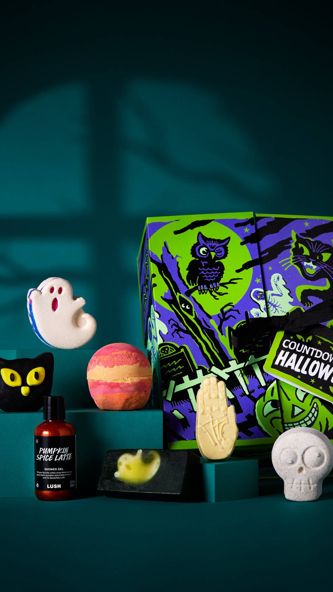 The image shows a colourful 'COUNTDOWN TO HALLOWEEN' gift box on a dark teal platform. Six products are arranged around it, including bath bombs, a bubble bar, a massage bar, a shower gel and soap. 