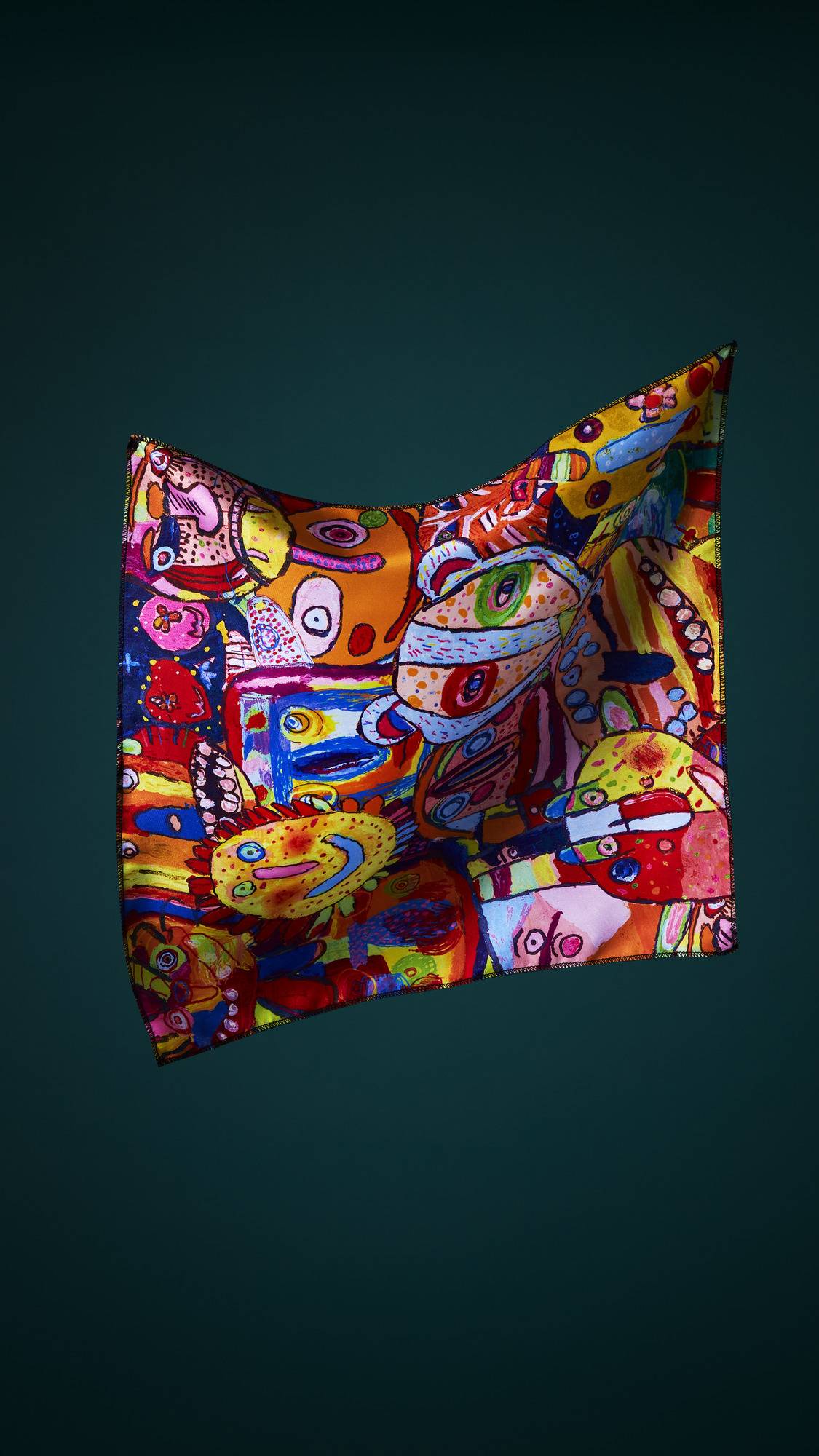 The image shows the square, multicoloured fabric Mischief Makers knot wrap, suspended in mid-air against a dark teal background. It features a chaotic collage of abstract monster faces in a variety of vibrant colours.