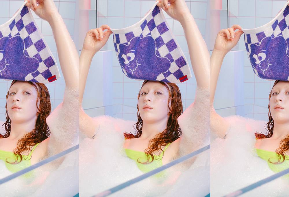A model raises the face cloth from their face whilst relaxing in the bath.