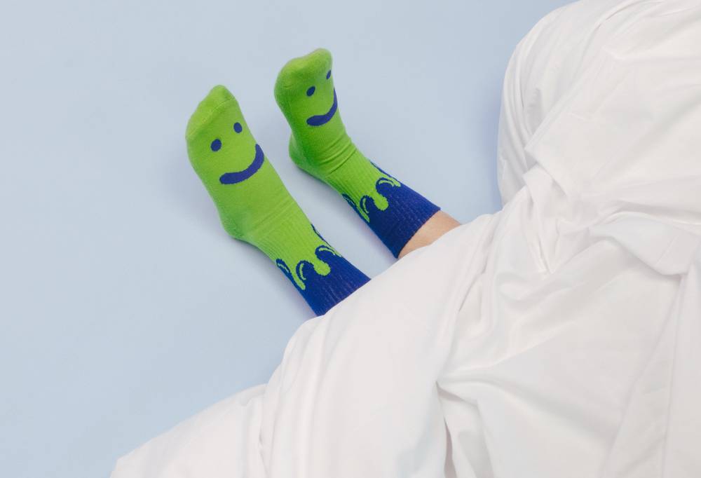 Green and navy blue happy face design socks, poking out from under a duvet.
