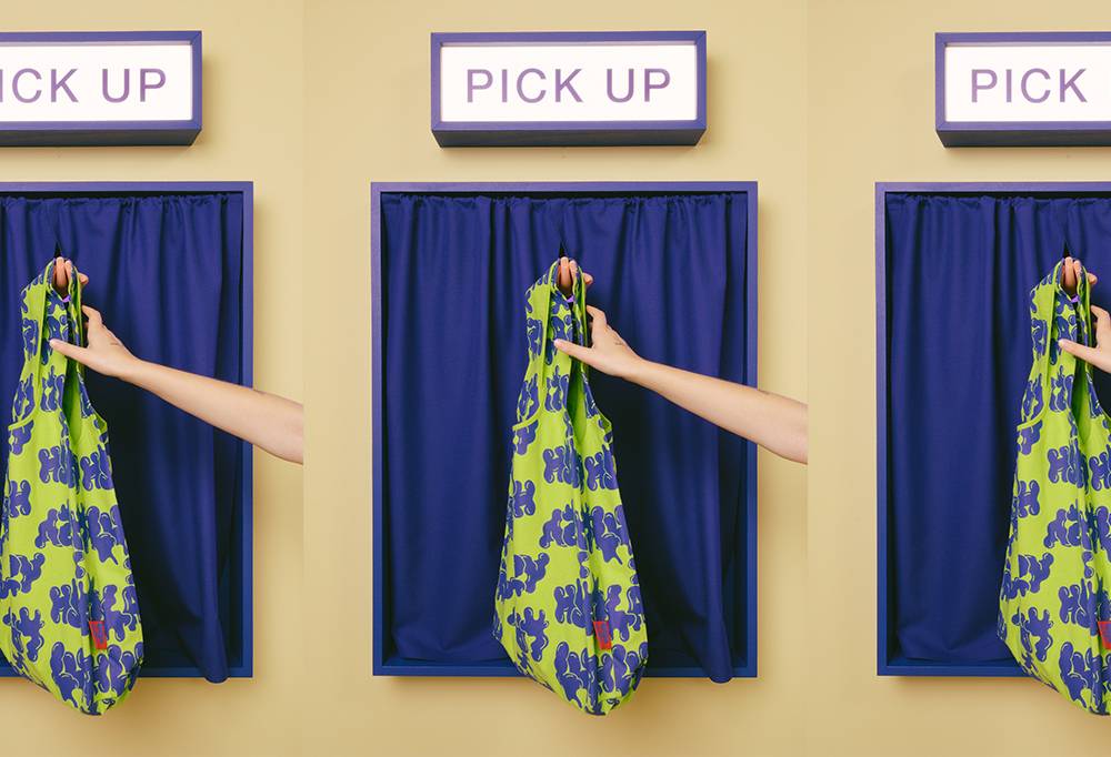 The Lush x Lazy carrier bag is handed to a model from behind a blue curtain.