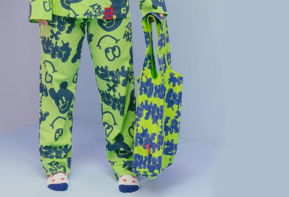 A model wears the full set of pyjamas and holds the green and navy blue Lush x Lazy carrier bag.