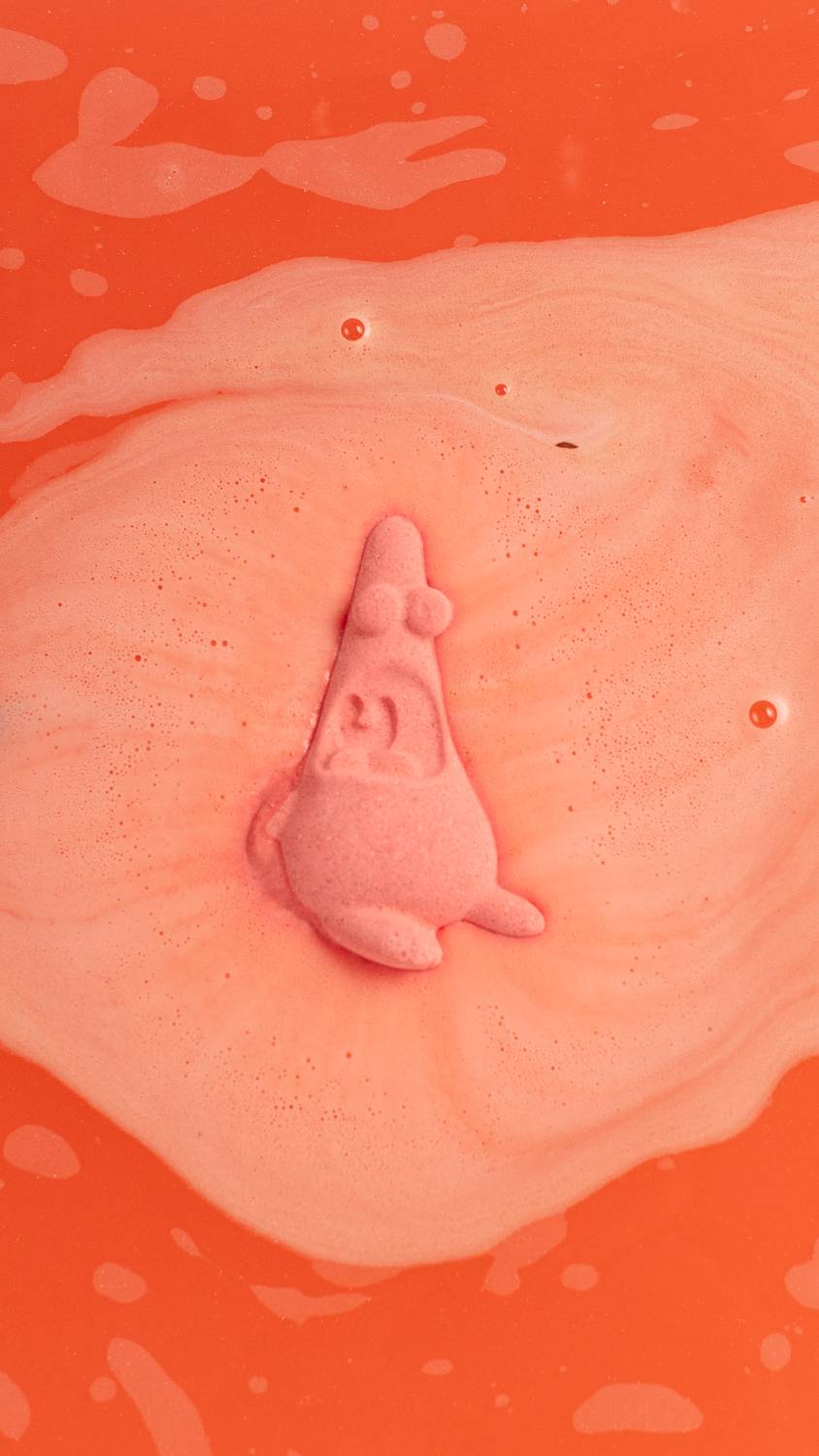 Surprised Patrick Bath Bomb sits among foamy swirls of deep coral pink.