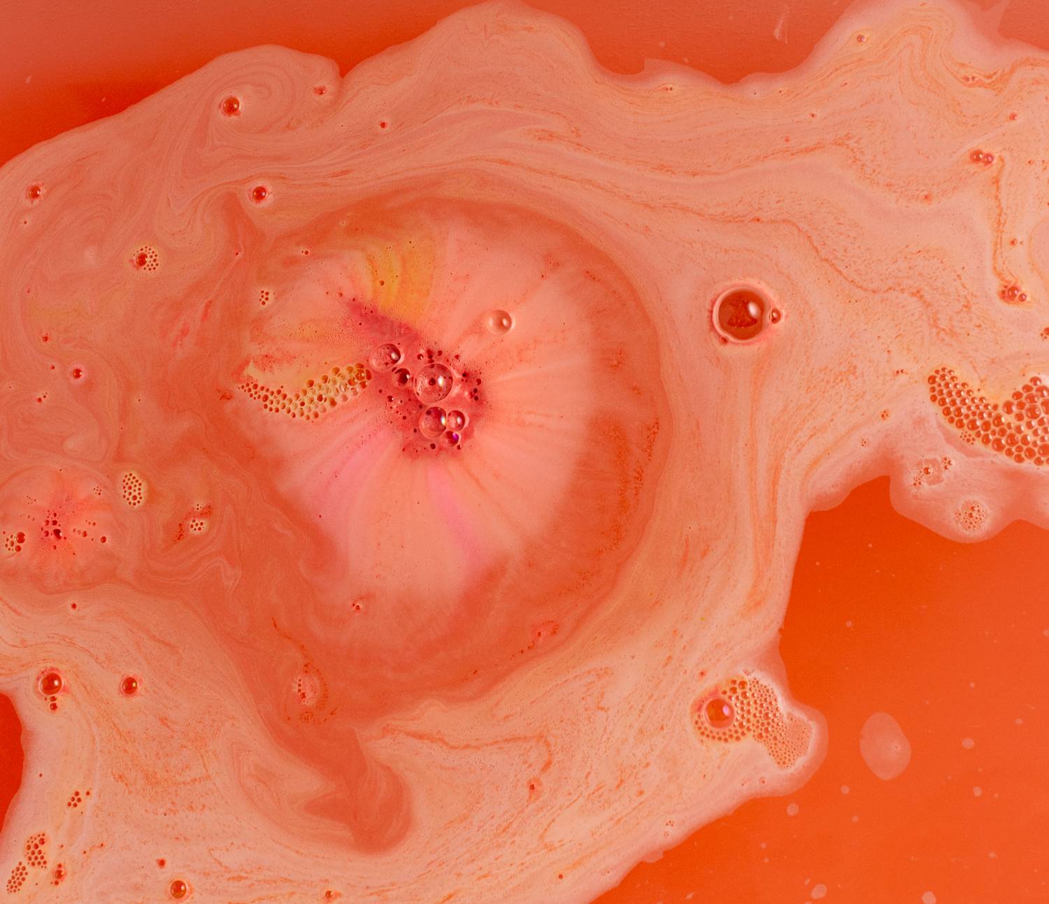 Surprised Patrick bath bomb fizzles among deep coral foam with hints of pink and orange.