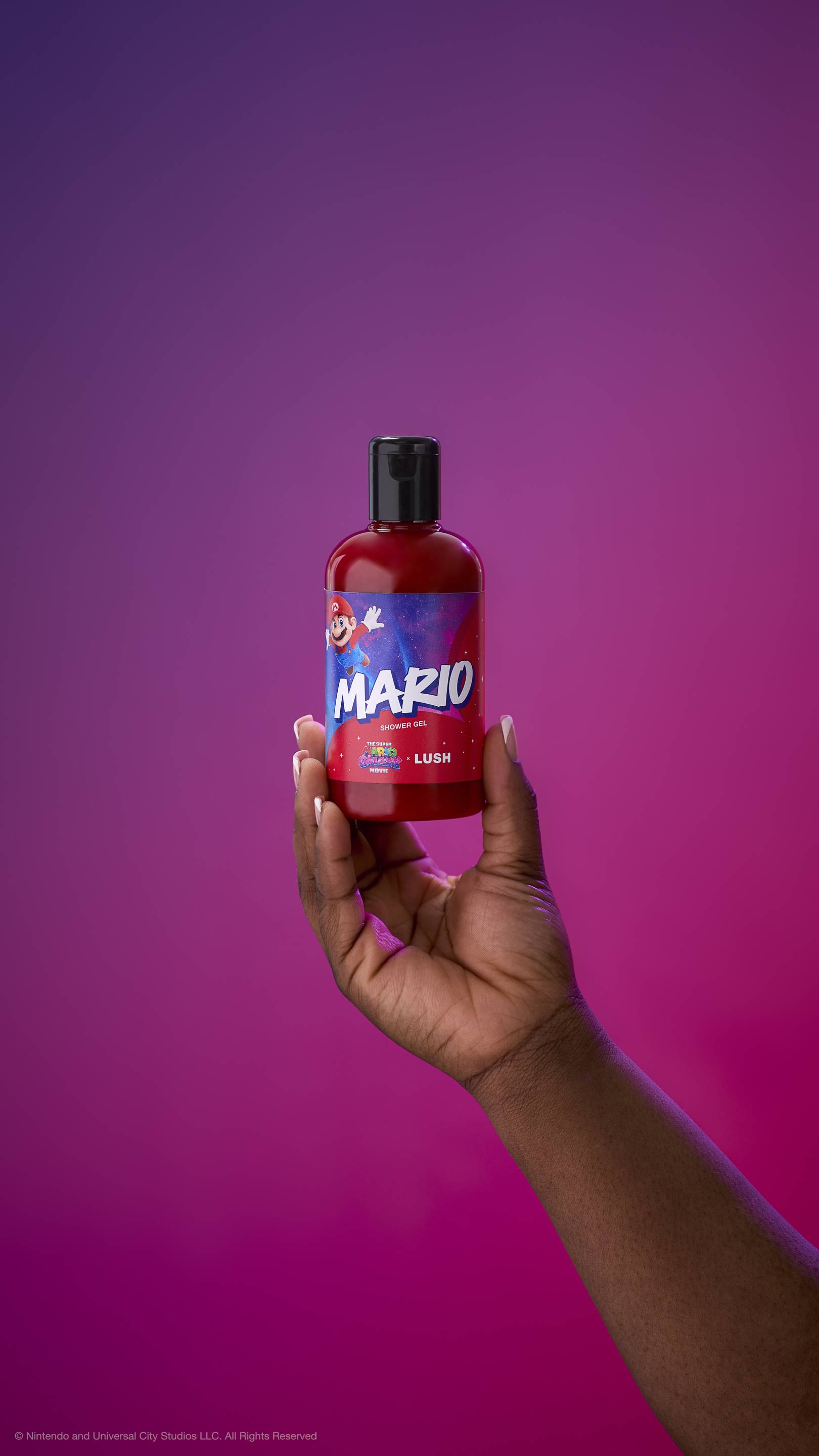 Hand holds a red Mario shower gel bottle with a black cap against a purple-magenta gradient background. The label features Mario jumping against a starry galaxy background with "MARIO SHOWER GEL" in bold letters.