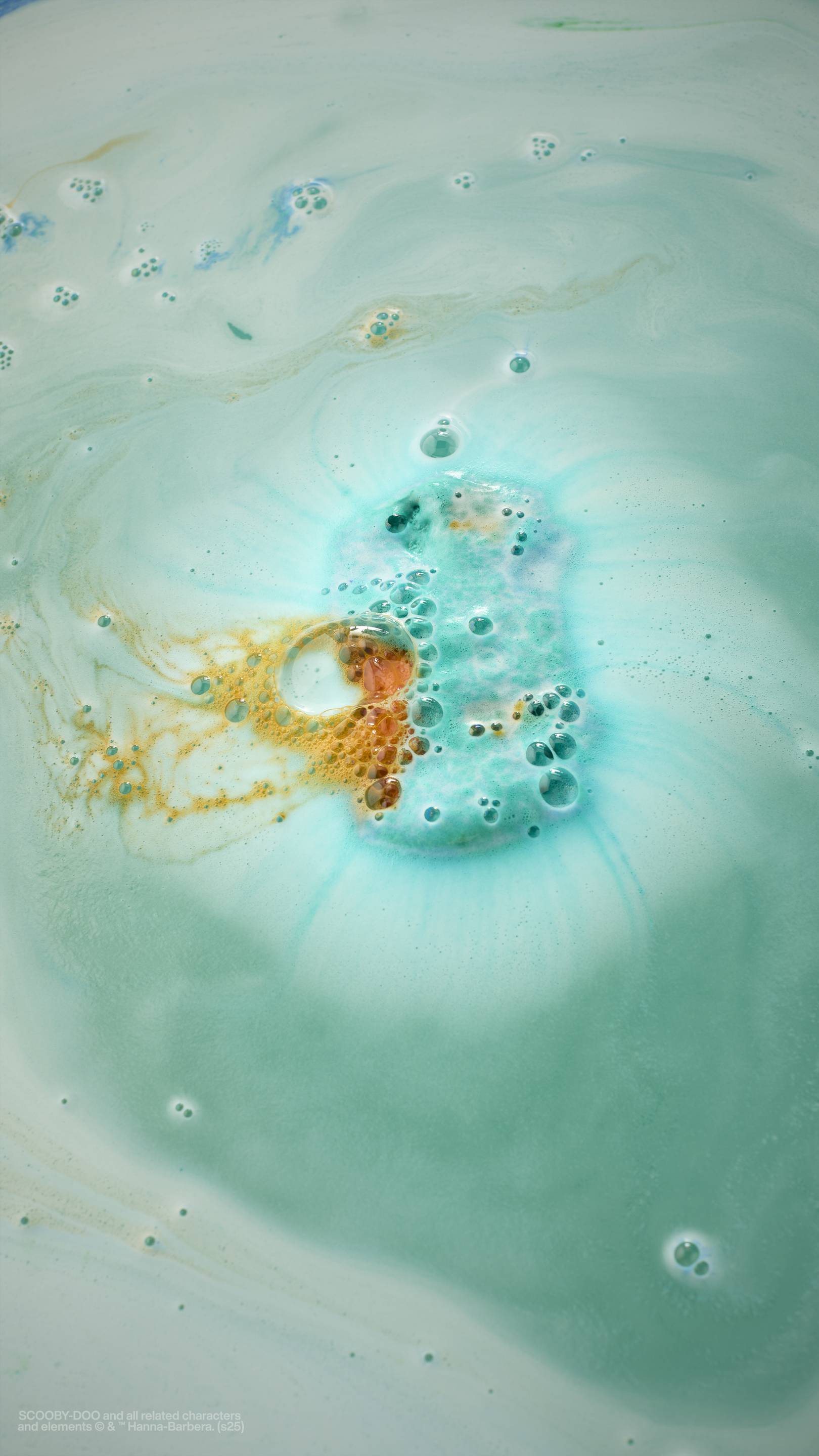 The image shows the bath art after using The Mystery Machine,  blue, orange and green bath bomb. The water is a teal colour,  coated in thin, velvety foam with tiny bubbles. There are ripples of blue and bright orange. 