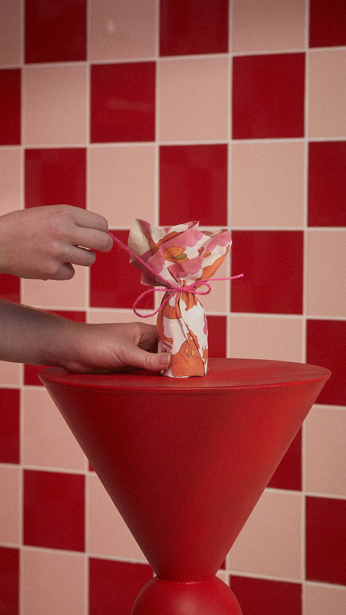 The image shows the Nuts For You gift wrapping around a Lush product, tied with pink string on a red table.