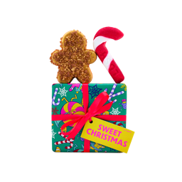A green festive-patterned Lush 'Sweet Christmas' gift box tied with a bright pink ribbon and yellow tag, displayed with a gingerbread-shaped bath product and a red candy cane bubble bar.