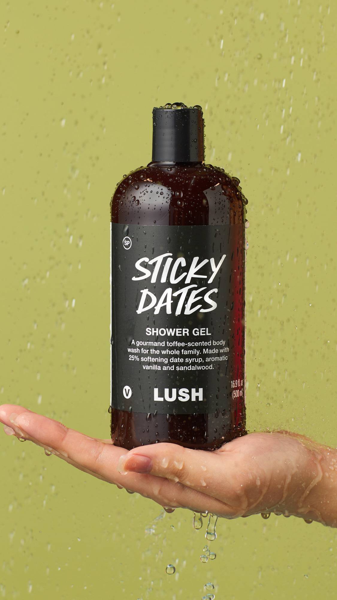 A hand holds a large bottle of "Sticky Dates" Shower Gel while water rains down on it against a light green background. The black label describes the product as a "gourmand toffee-scented body wash" containing date syrup, vanilla, and sandalwood.