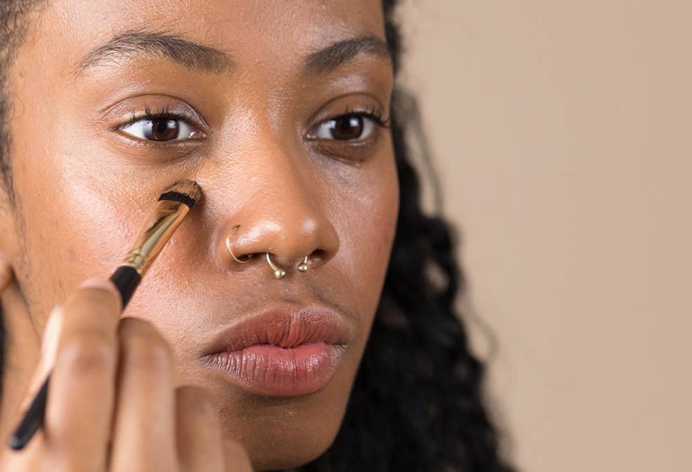 A person appears focused, as they get To The Point, a small concealer brush, working with concealer in the under eye area.