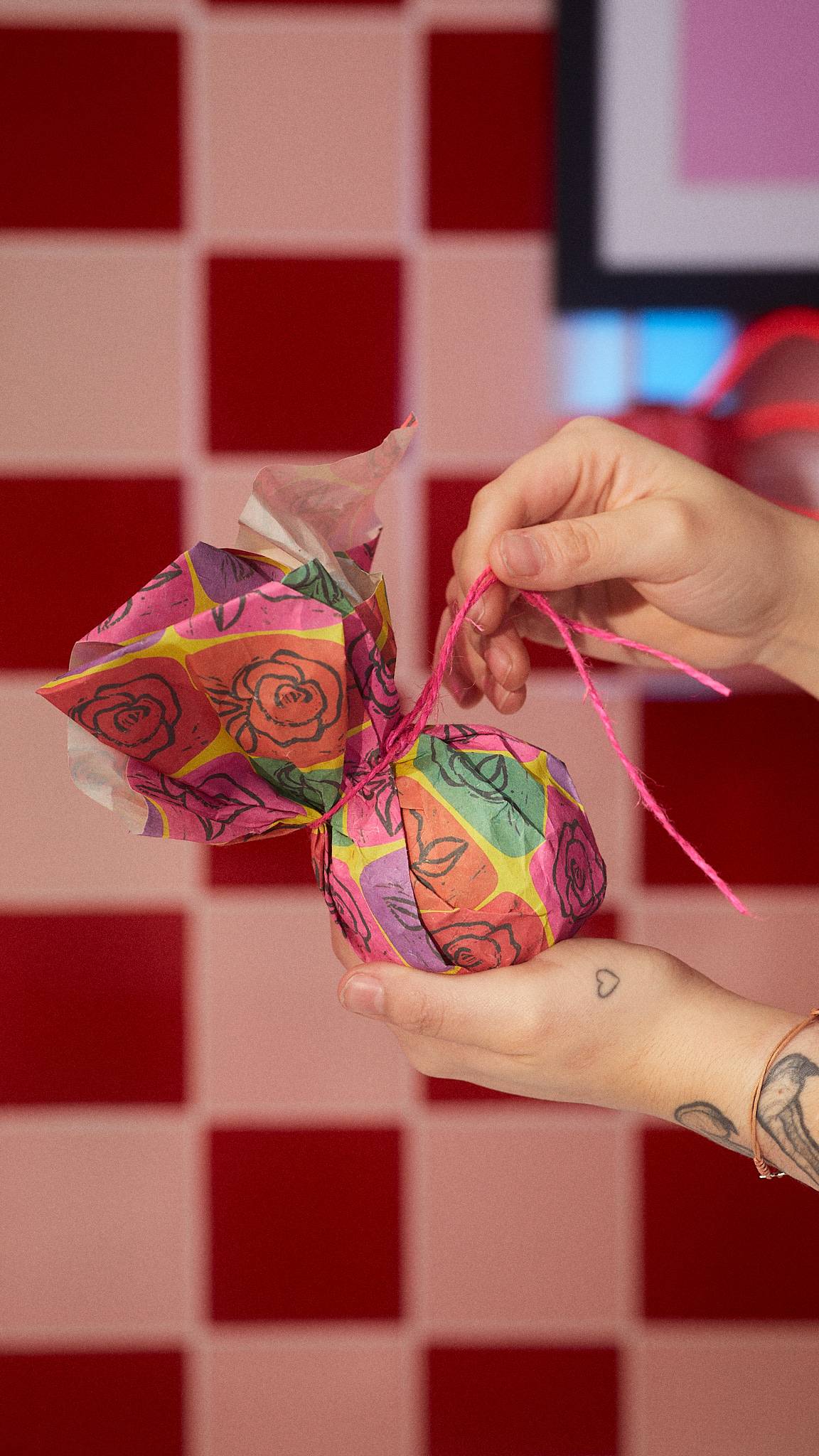 A close-up of the model holding a wrapped bath bomb in the Abstract Roses wrapping as they tie it with pink string.