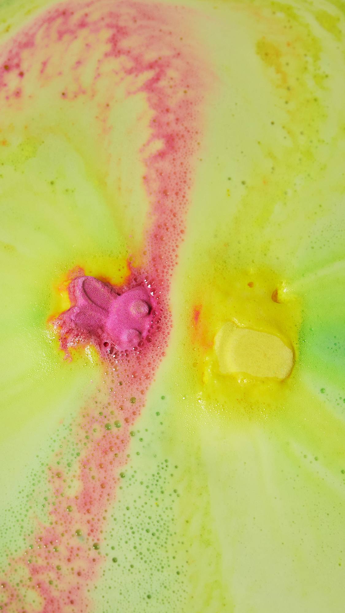 The bath bomb has mostly dissolved leaving a sea of velvety pink, yellow and green foam. Part of the pink bunny face is still visible through the foam.