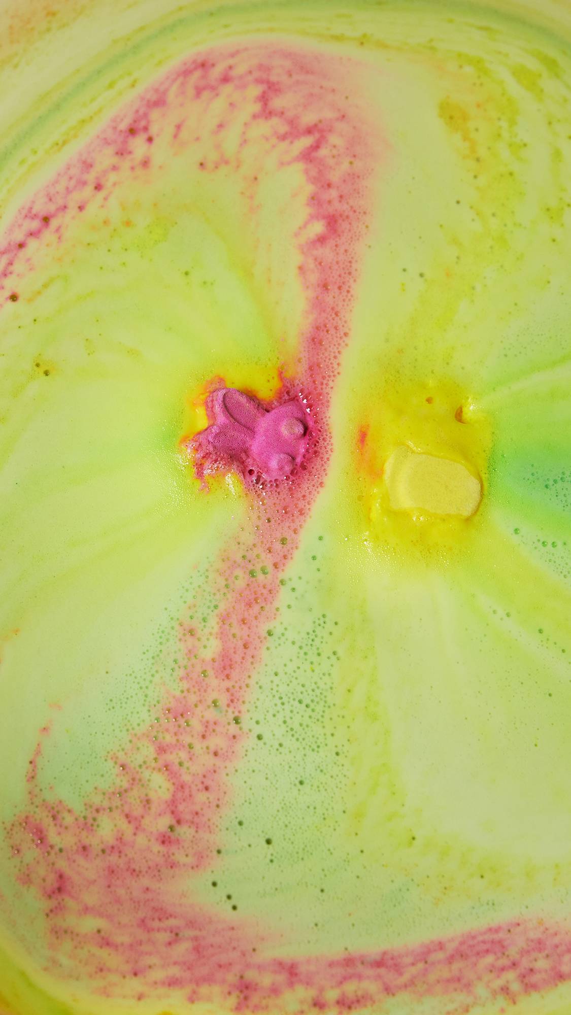  The bath bomb has mostly dissolved leaving a sea of velvety pink, yellow and green foam. Part of the pink bunny face is still visible through the foam.