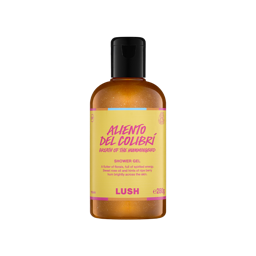 A clear bottle filled with shimmering, golden-amber Lush Aliento del Colibrí shower gel, topped with a black cap and featuring a bright yellow label with pink text