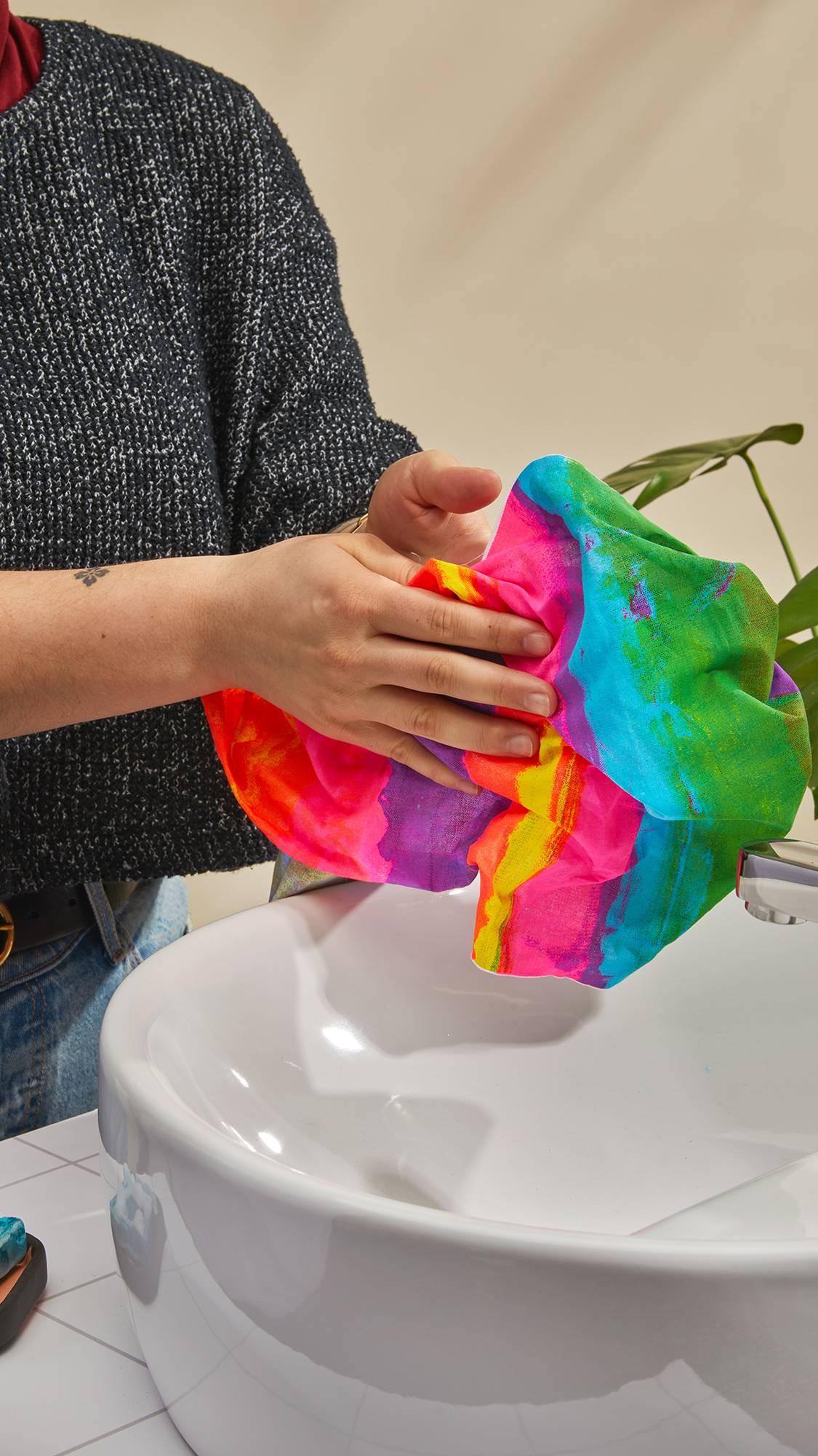 The image shows the model stood at the sink drying their hands with the All The Colours Tenugui knot wrap after having just washed their hands. 