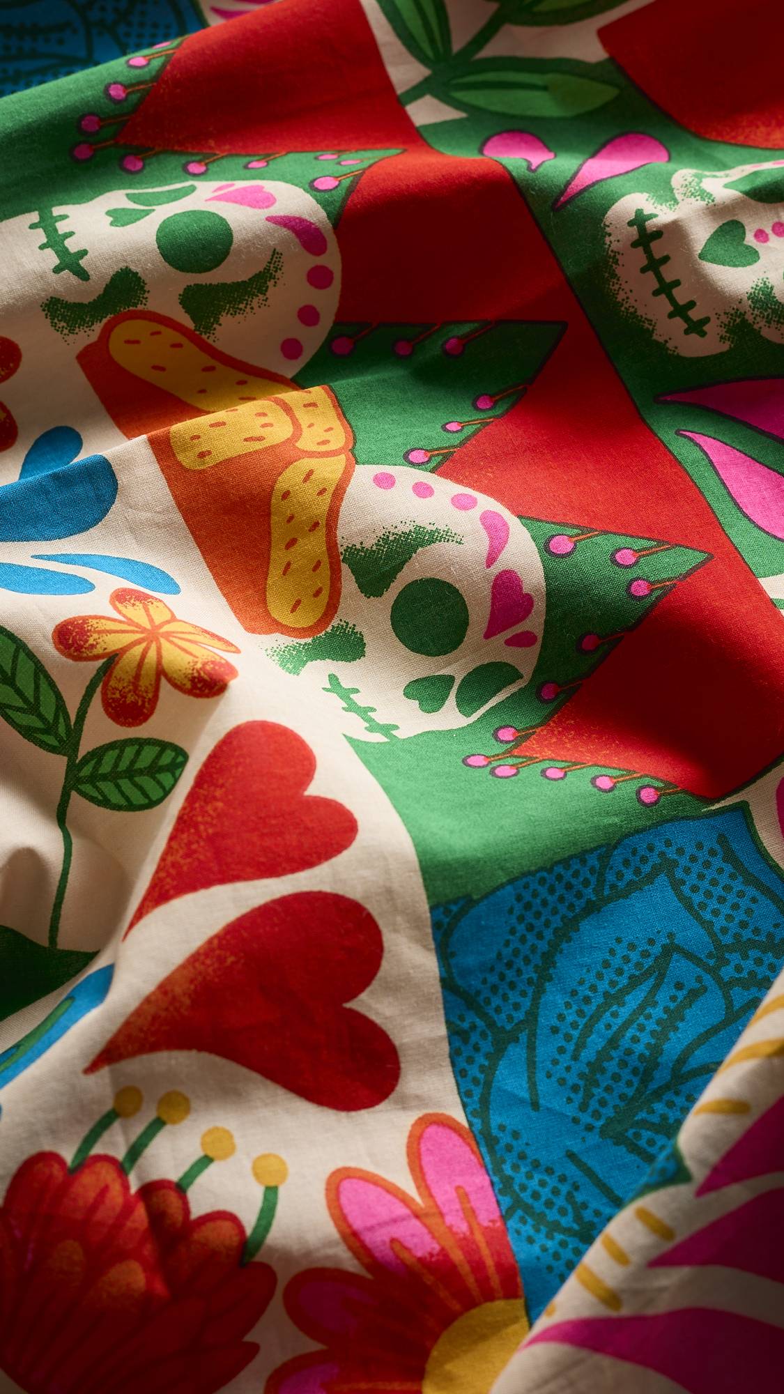 A super close-up image of the Dia De Muertos-themed, Amor Eterni fabric knot wrap. It focuses on the material texture, softness and colour vibrancy of the fabric wrap. 