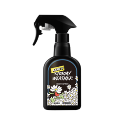 A Lush body spray bottle in a matte black trigger-spray container. The label reads "A&Ne's Stormy Weather" in stylised text, featuring a cartoon flower character amidst white daisies. Logos for Lush and Aki & Friends are at the bottom.