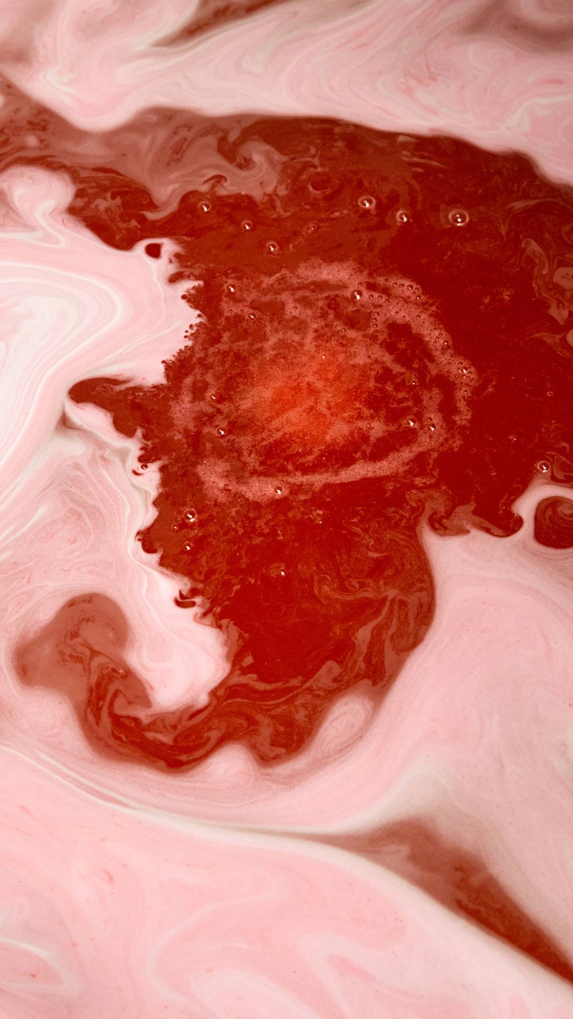 The Apple A Day bath bomb has completely dissolved leaving behind deep, garnet-red waters with delicate, light foam scattered on top.