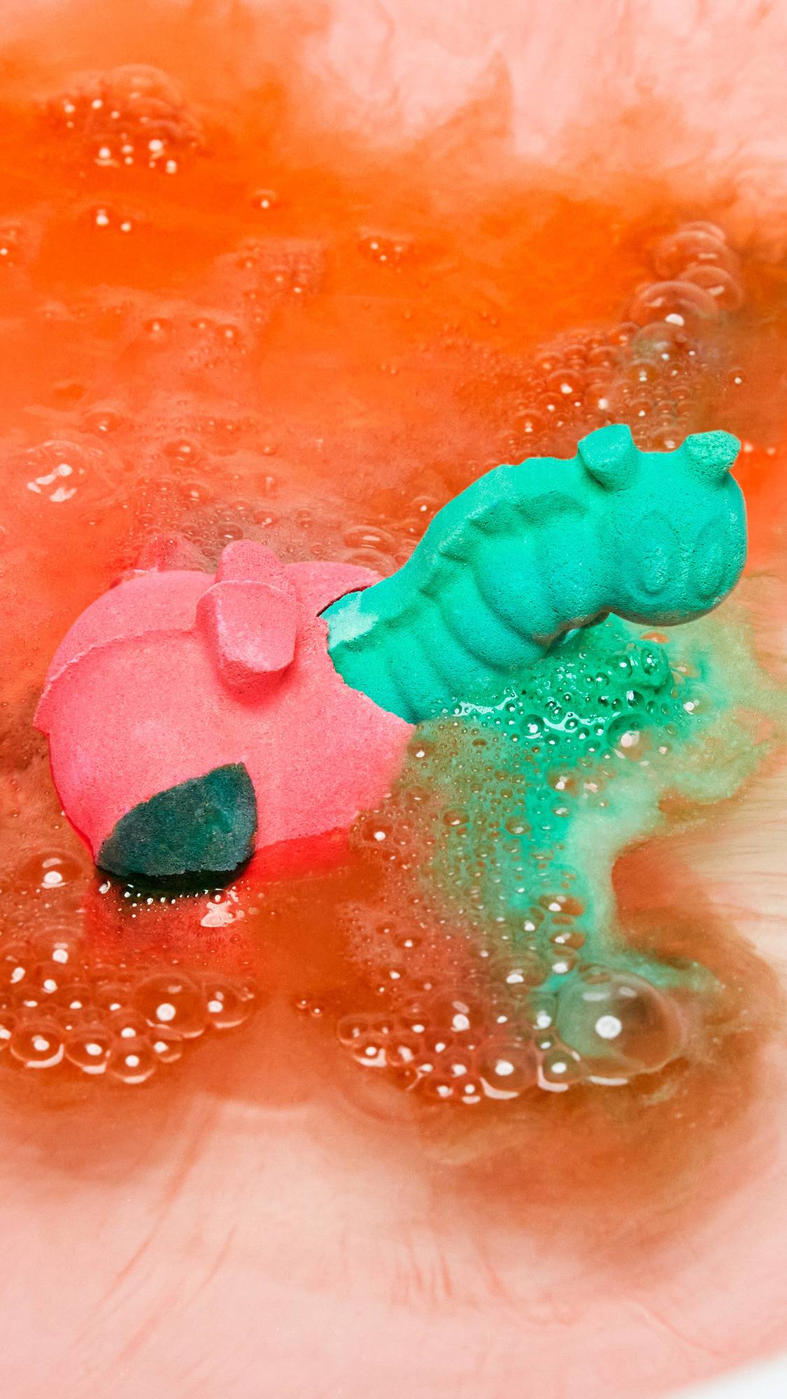 The Apple A Day bath bomb has been gently placed into the bath water as it begins to disperse velvety ribbons of red and green foam. 