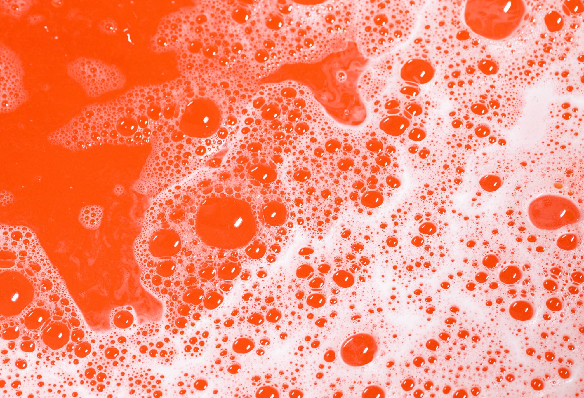 Vivid red water with a covering of bubbles of all different sizes, dotted in white foam.