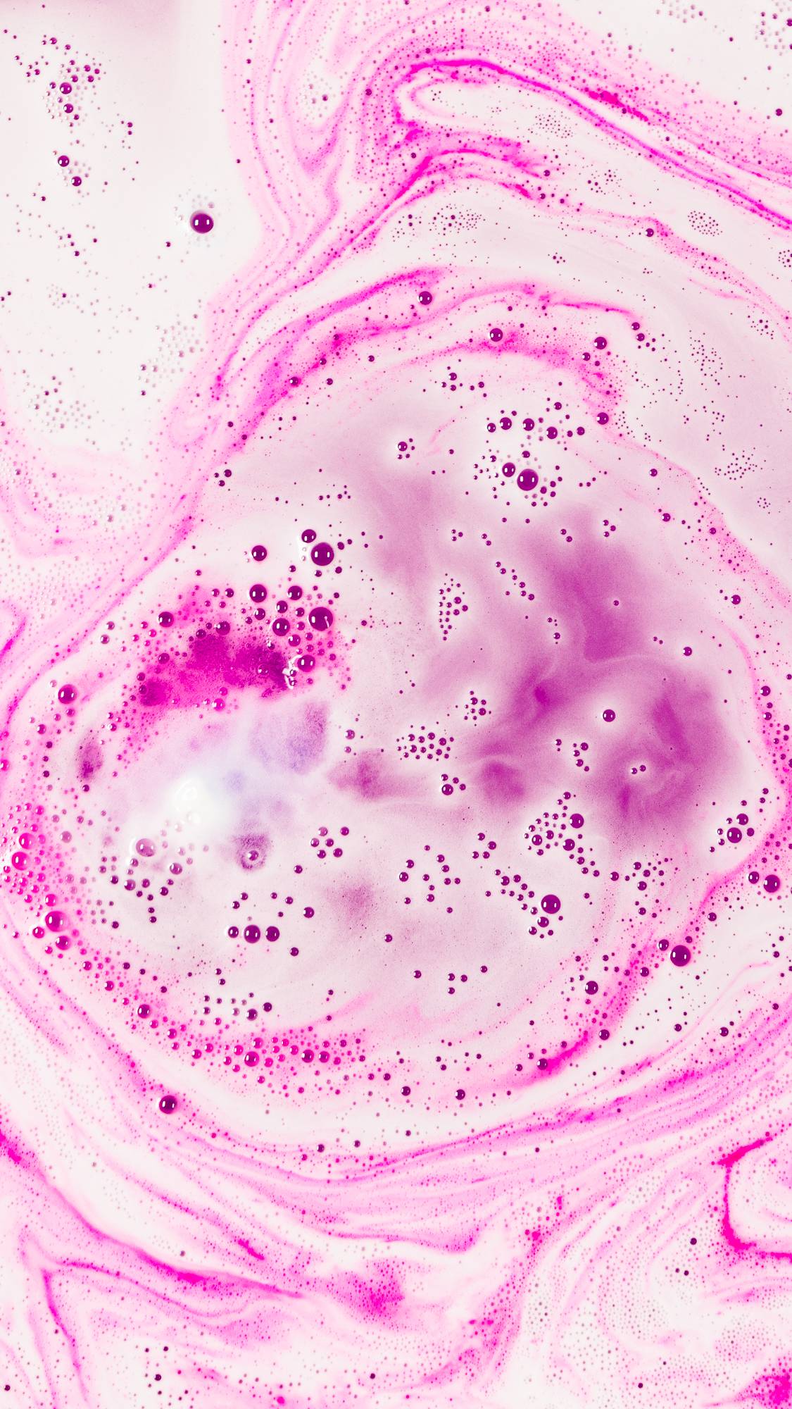 The Atom Heart Mother bath bomb has fully dissolved leaving vivid pink,  foamy swirls.