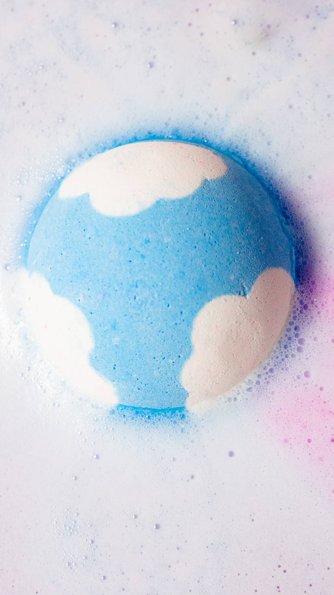 The Atom Heart Mother bath bomb sits in the water slowly dissolving, giving off thick foam and hints of pink.