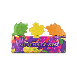 Three leaf-shaped bath bombs in green, yellow, and orange sit on top of a rectangular box featuring a vibrant, colourful leaf pattern and gold text that reads "AUTUMN LEAVES".