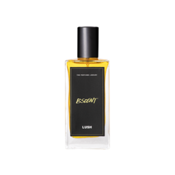 A glass perfume bottle filled with amber liquid. A black label reads 'The Perfume Library' and 'B Scent'.