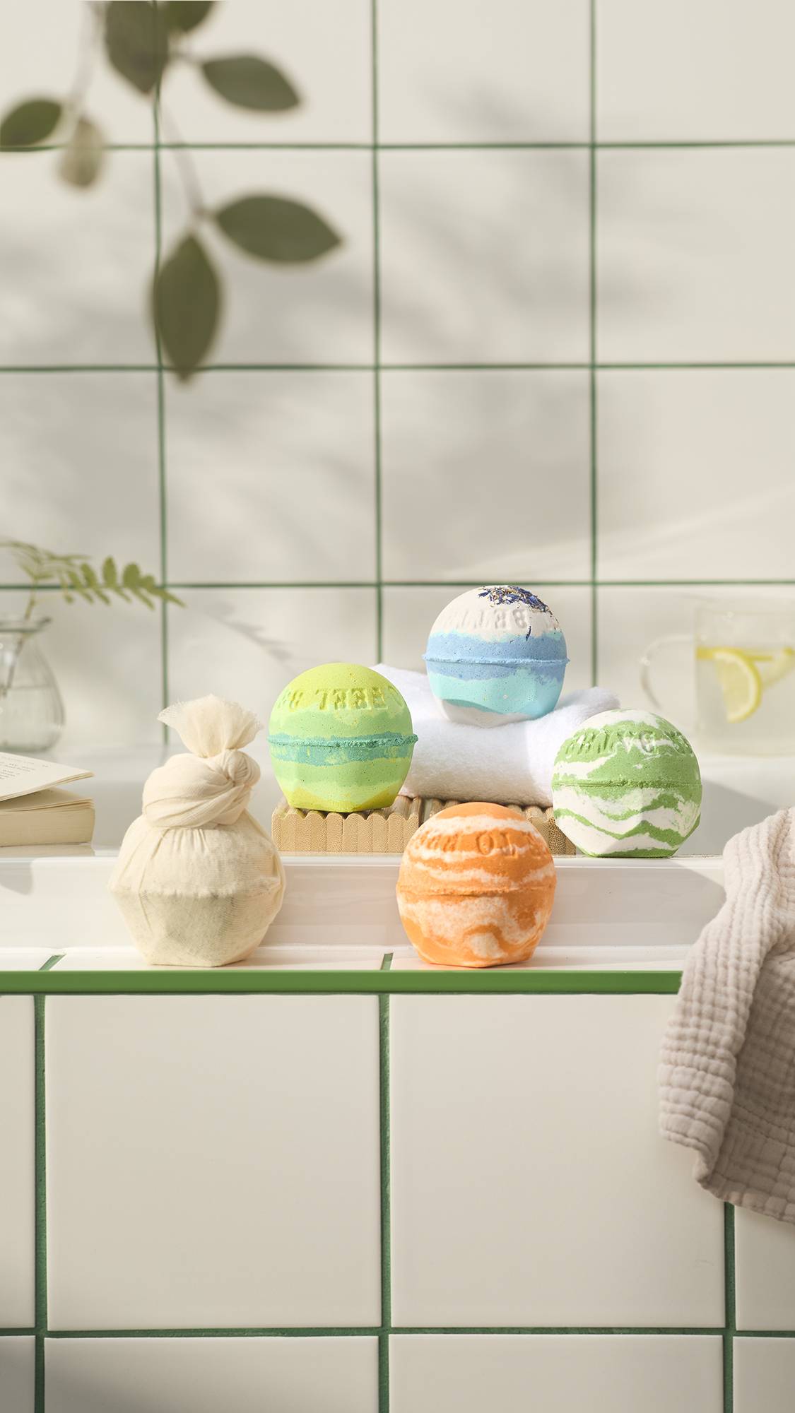 A selection of five colourful, spherical bath bombs, part of the LUSH "Bathe To Feel Better" range, including "This Too Shall Pass", "Dream Cream Soak", "Bather's Digest", "Byegraine" and "Cold, sat on a tiled ledge in a bright bathroom.