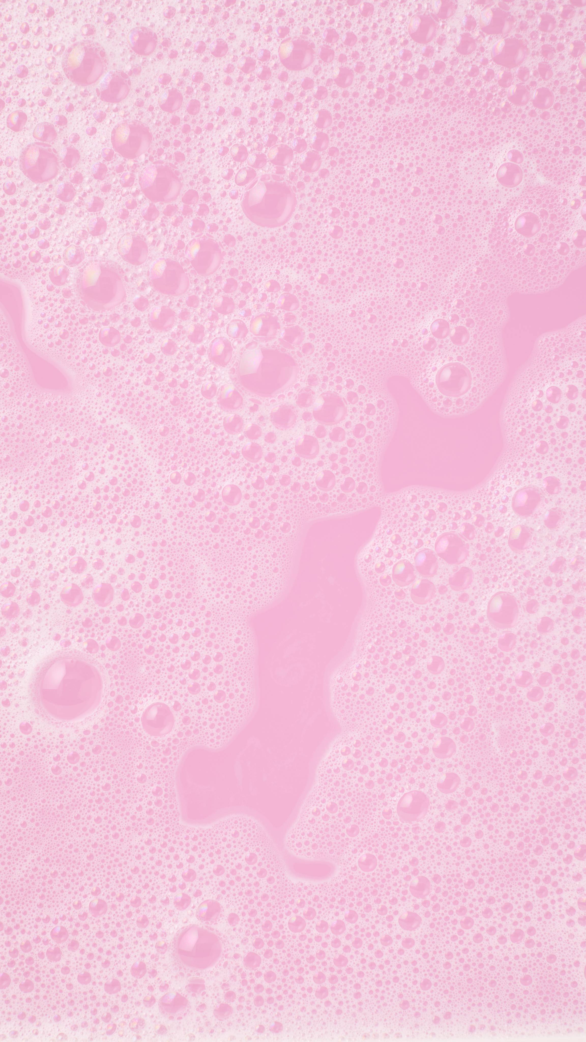 A close-up, aerial view of a thick layer of pale pink bubbles and foam covering the surface of the bathwater, created by the Be My Valentine bubble bar. The bubbles vary in size, creating a dense, frothy texture with soft pink hues.