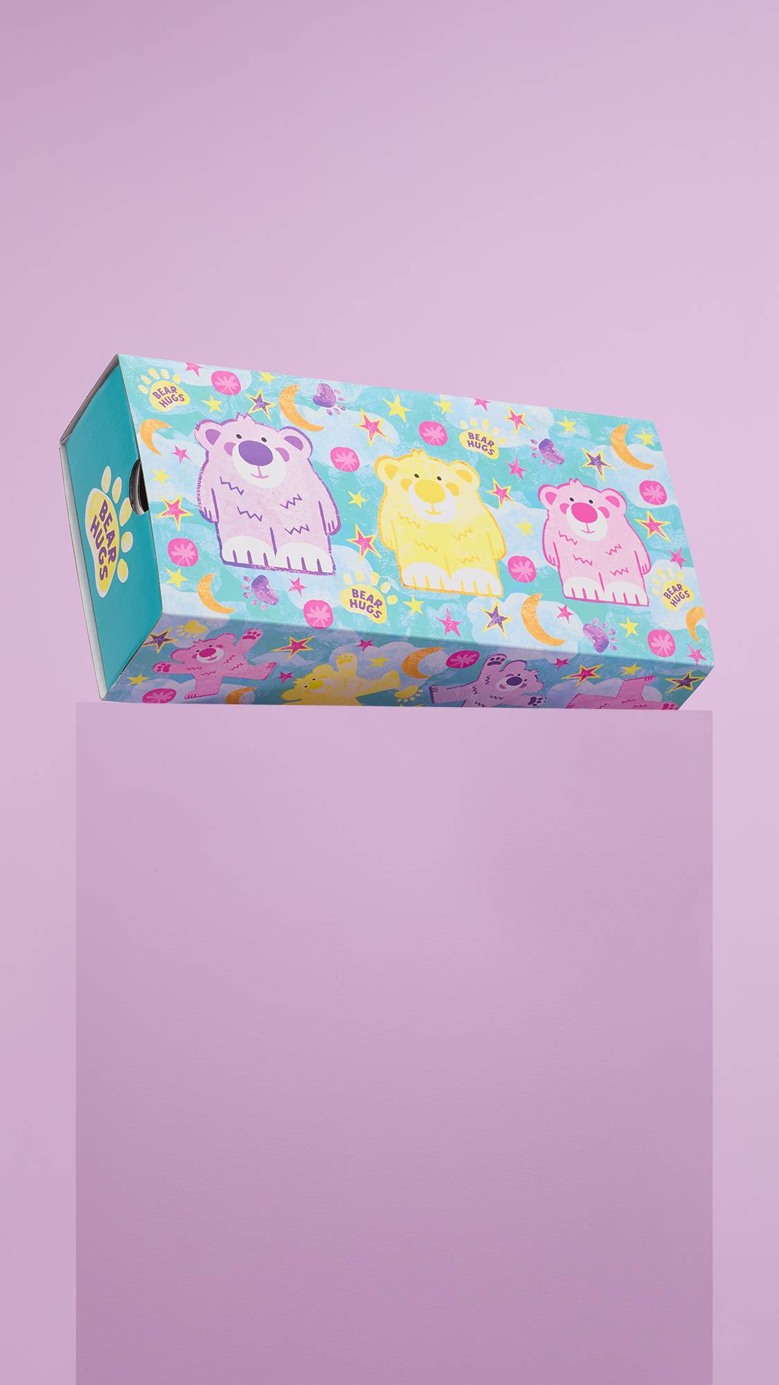 The image shows the colourful Bear Hugs, cardboard gift box, sitting on a dusky pink platform against a matching pink background. 