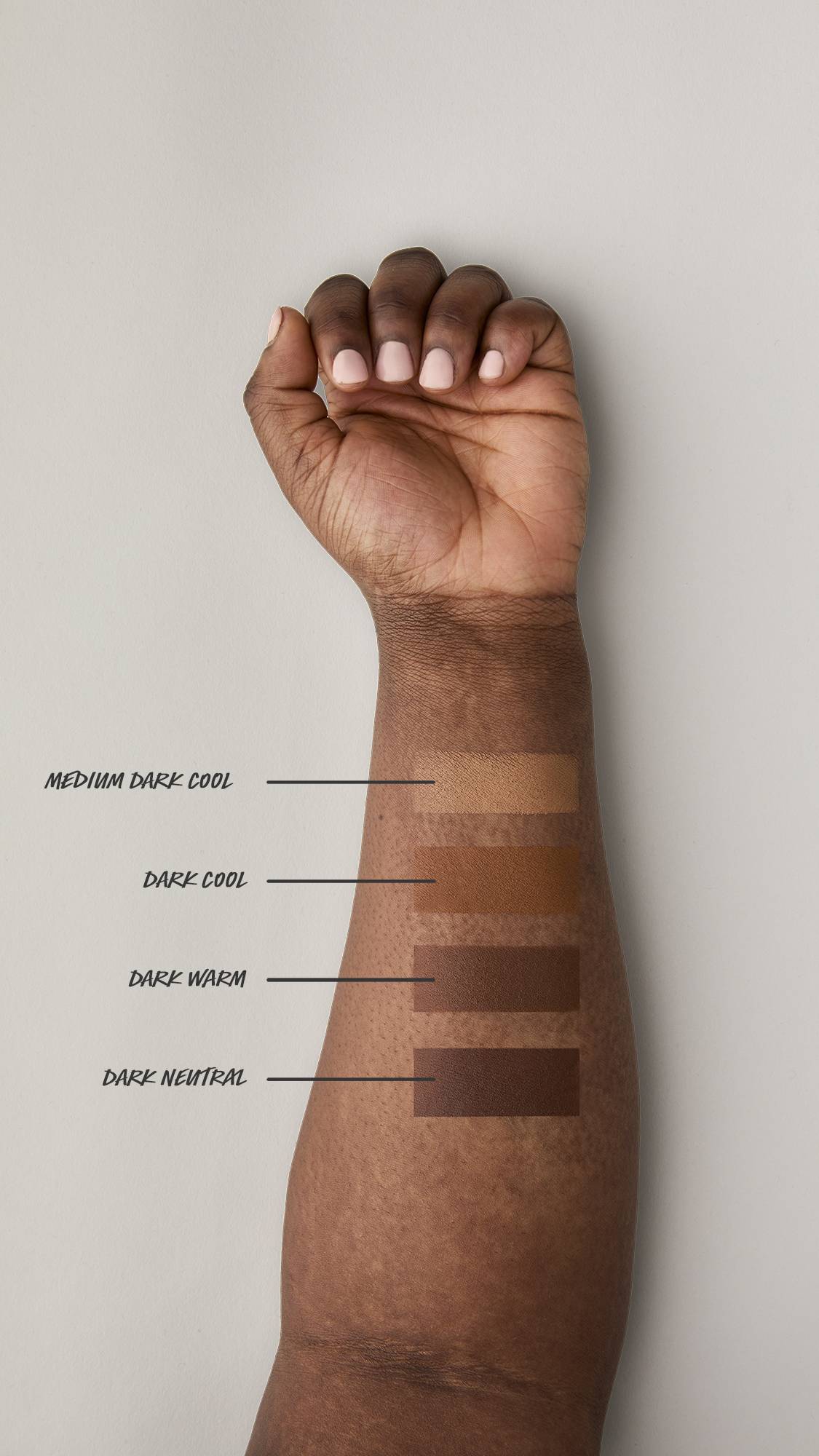 Four swatches of beauty balm are applied to the underside of a dark-skinned model’s forearm. Shades are listed from top to bottom: Medium Dark Cool, Dark Cool, Dark Warm, and Dark Neutral, showing a gradient of swatches against the dark skin tone.