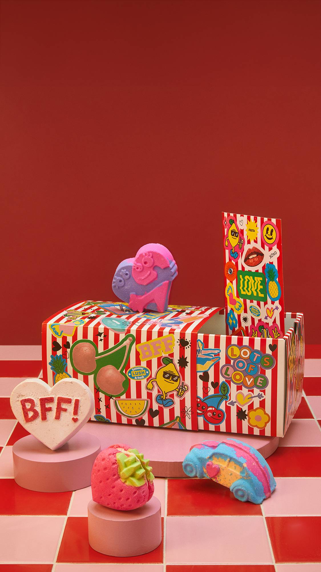 Image shows a red background with tiled flooring. On top of three small pedestals sits the BFF gift box with 4 bath products and a gift card. 