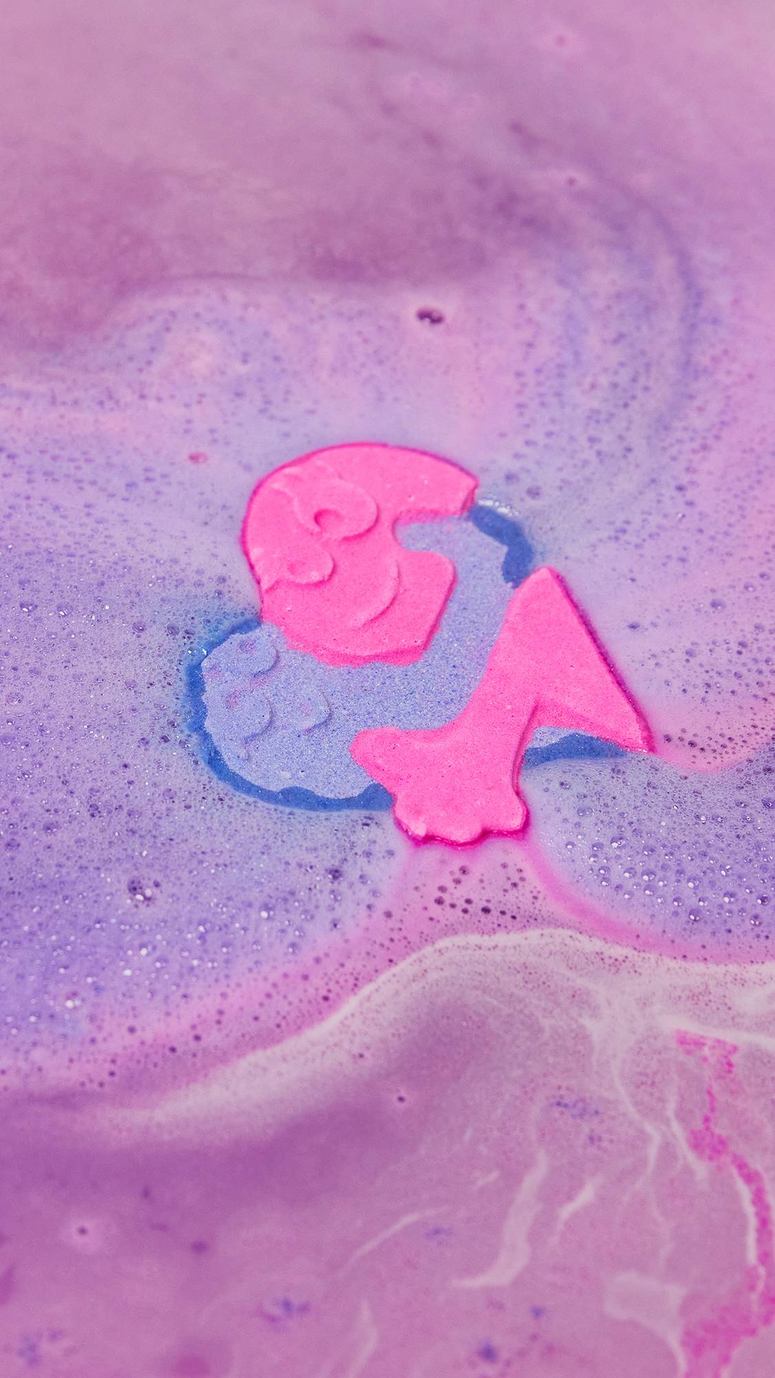 The Big Squeeze bath bomb is in the water dispersing velvety, deep pink and purple foamy swirl.