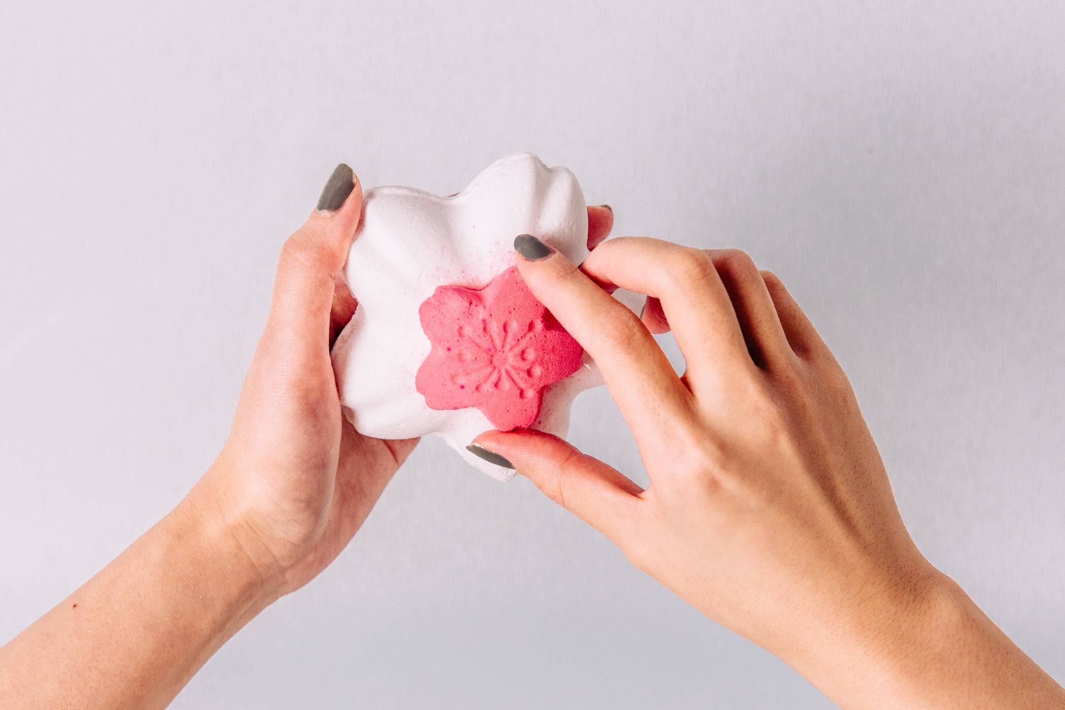 A close-up image of the mode's hands as they begin to separate the deep pink lip from the white main bath bomb body.