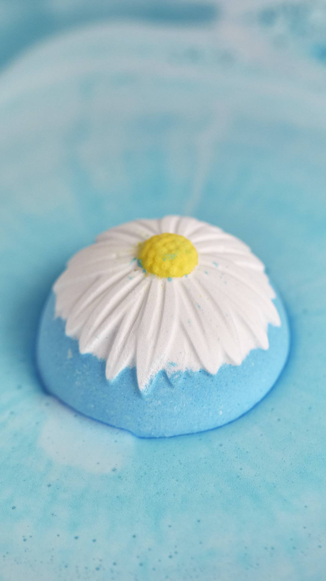 The image shows the view from above as the Blooming Beautiful chamomile bath bomb sits on blue waters. 