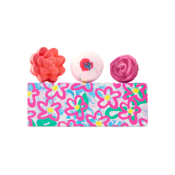 The Blooming Beautiful gift features a rectangular box with a pink and blue floral pattern. Three bath products sit on top: a comforter rose bath bomb, equity bath bomb, and a rose jam bubble bar