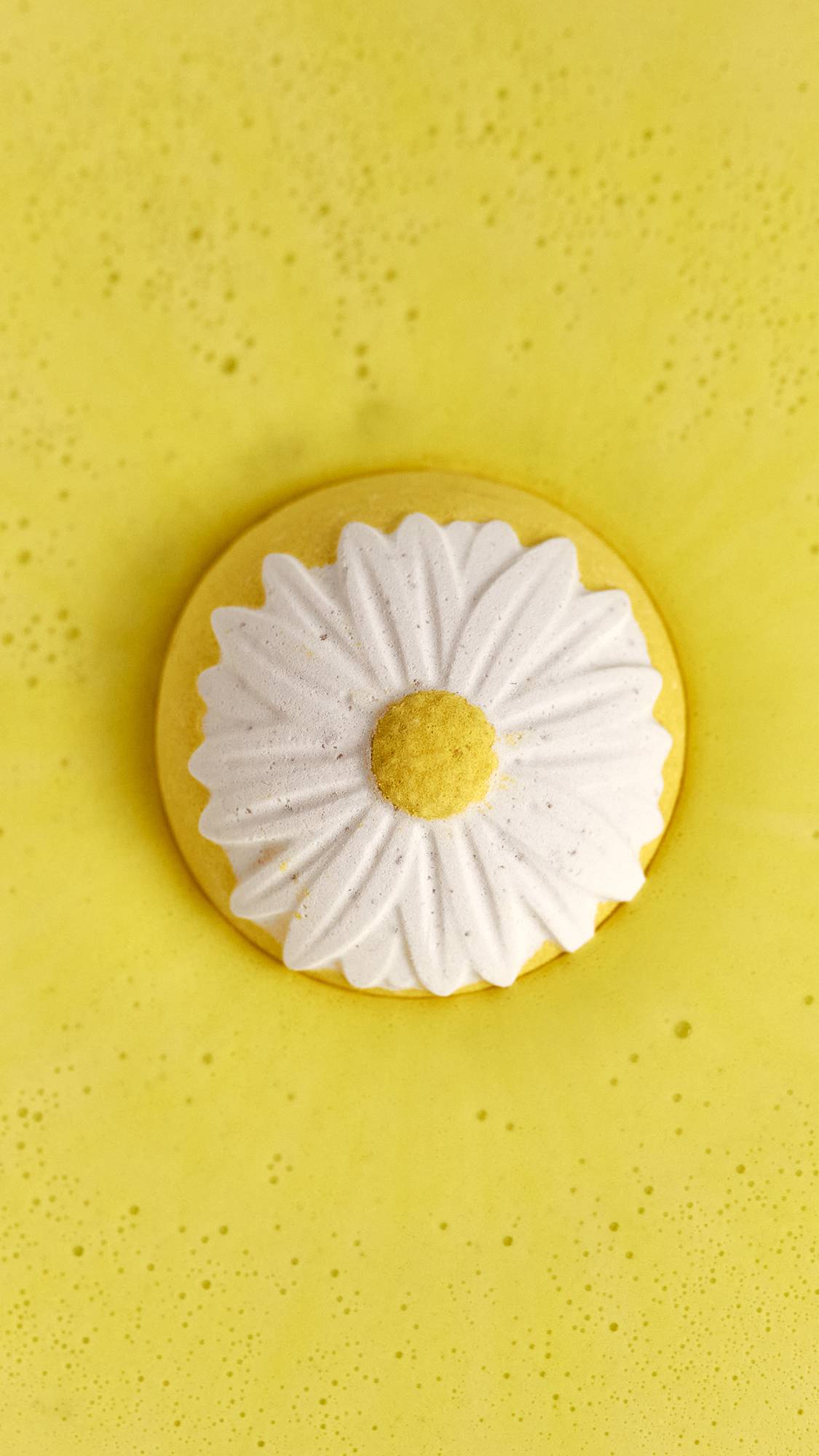 The image shows the view from above as the Blooming Beautiful Marigold bath bomb sits on vivid, yellow, foamy water. 