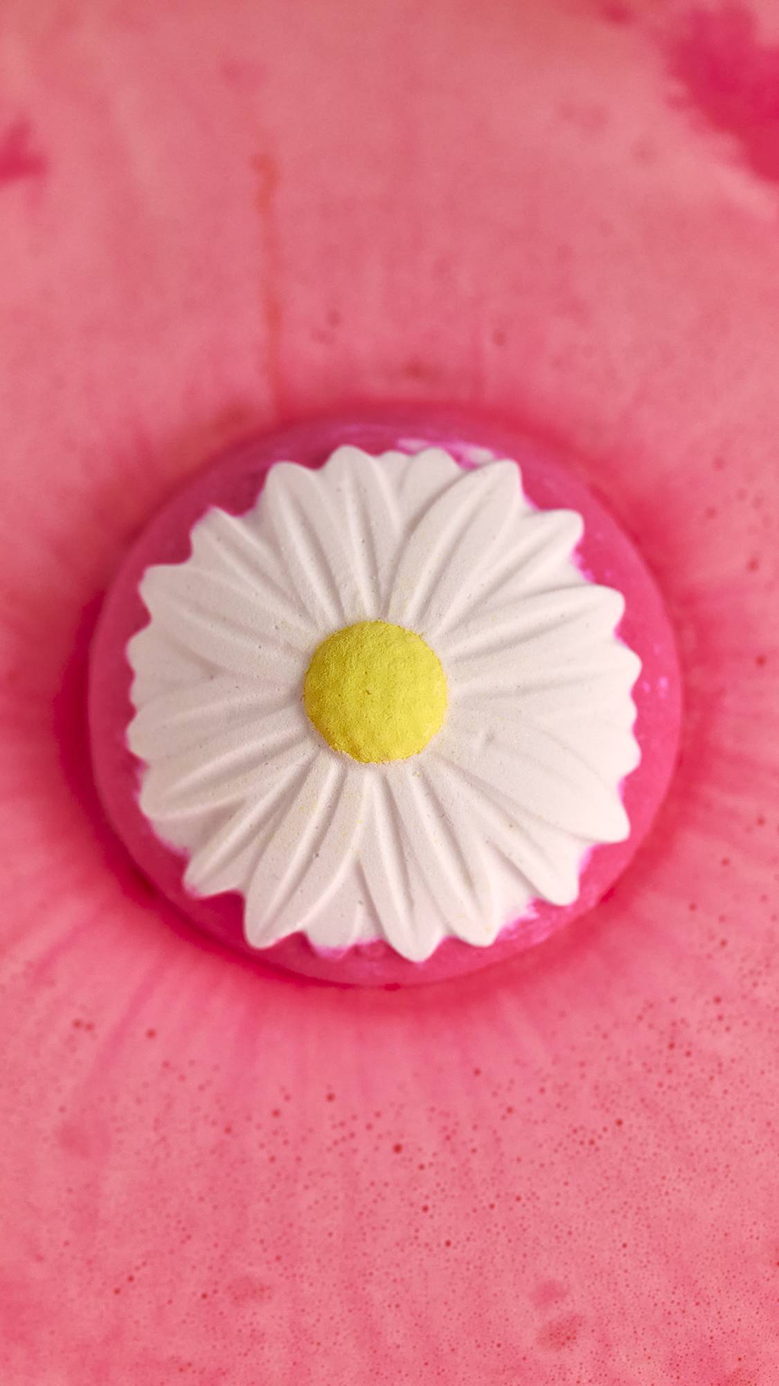 The image shows the view from above as the Blooming Beautiful Orange Blossom bath bomb sits on coral-pink waters. 