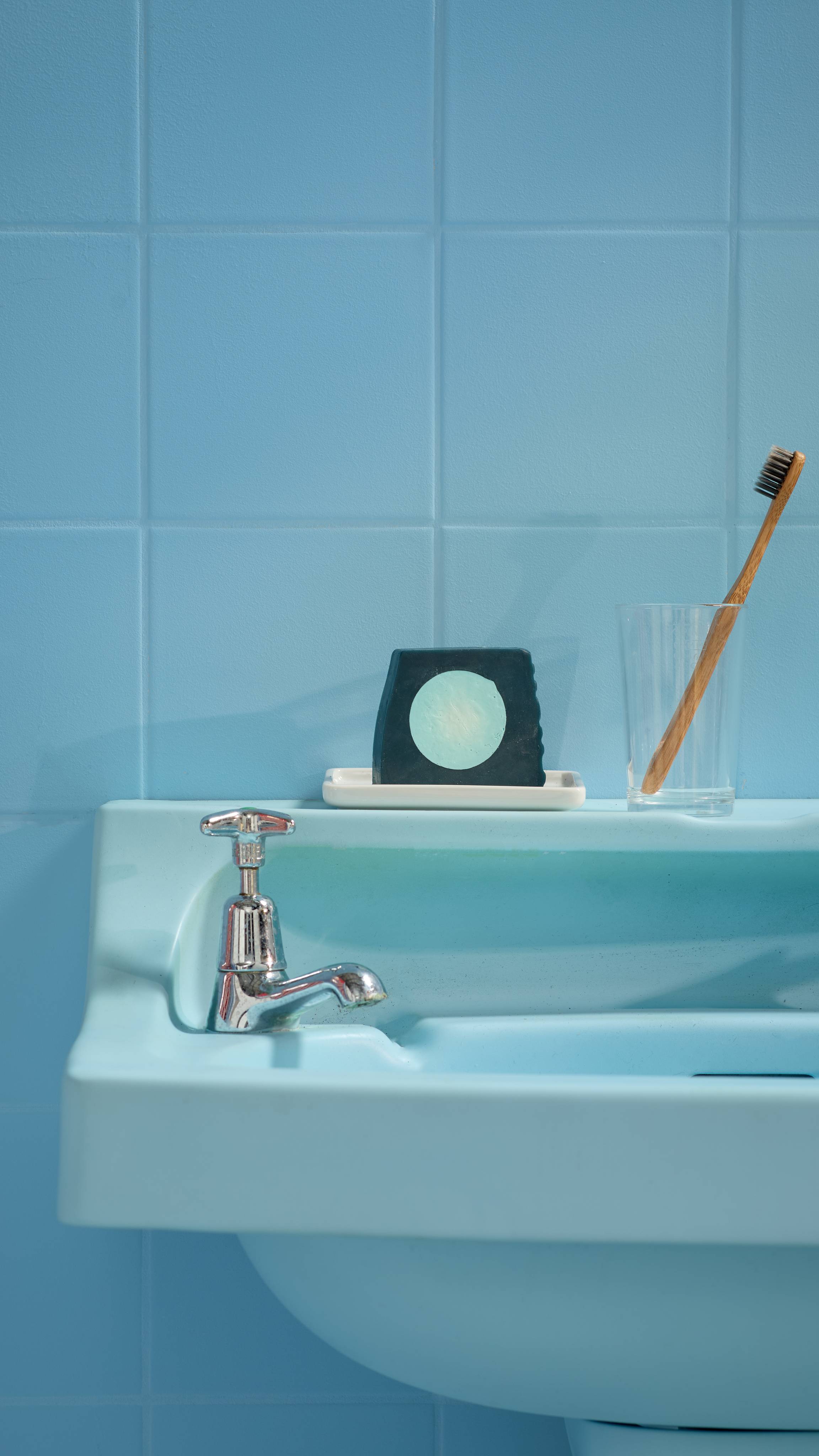 The image shows a blue, tiled bathroom with a matching blue sink. The Blue Moon soap is sitting on the side of the sink on a white soap dish. 