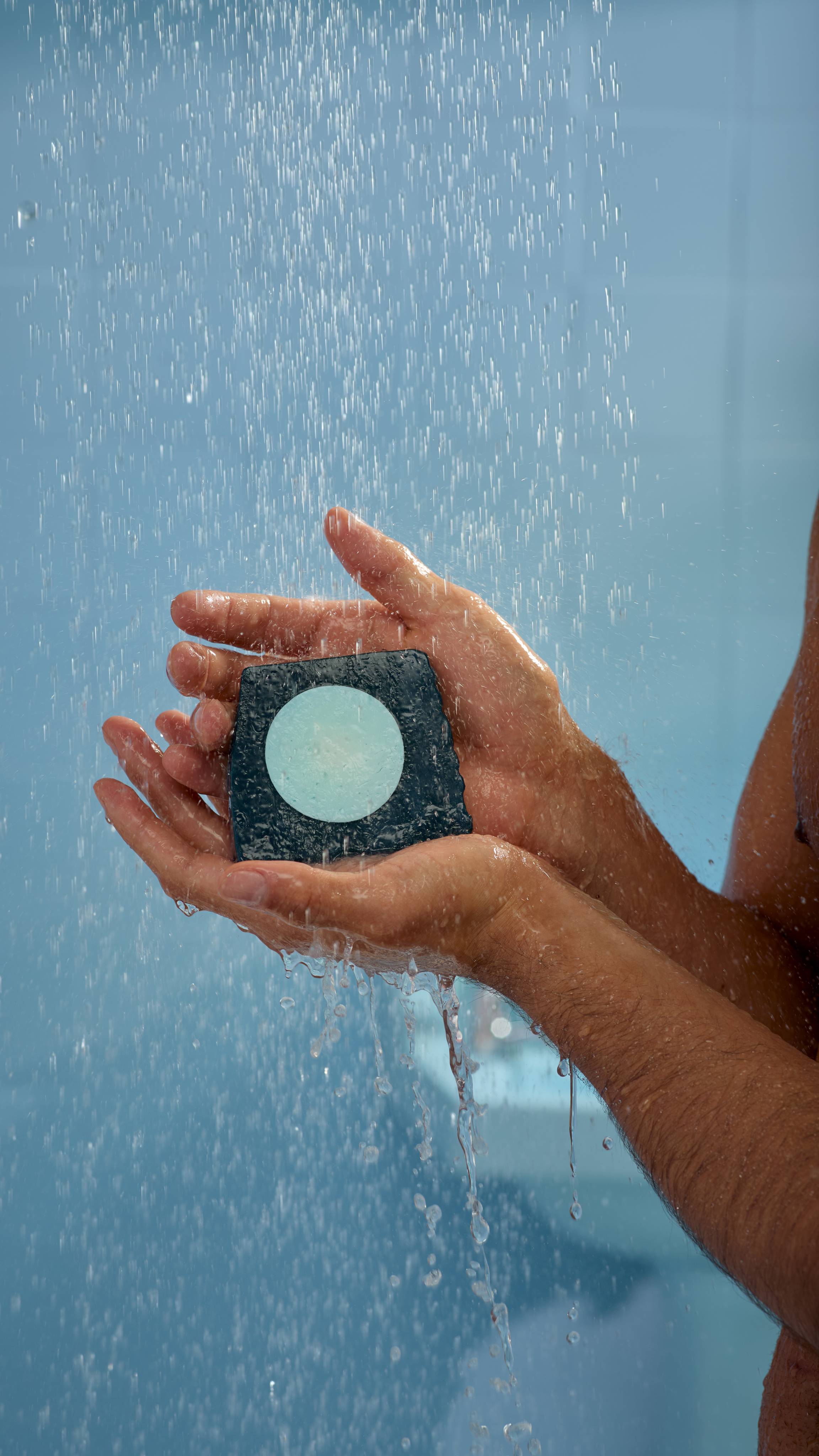 A close-up image of both of the model's hands gently holding the soap underneath running shower water. 