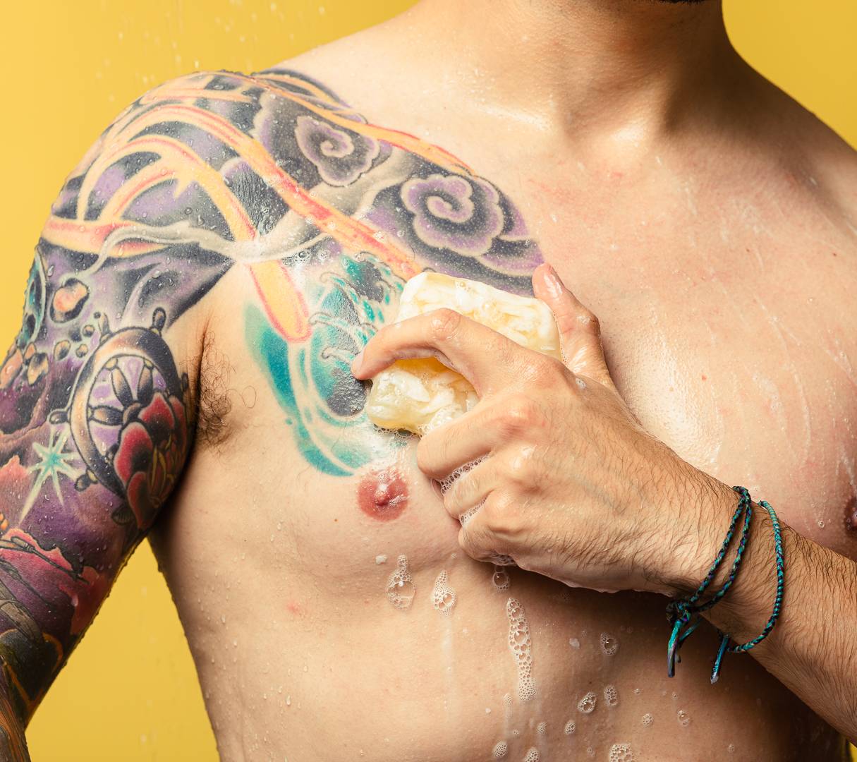Bohemian, a light yellow, creamy swirled, smooth soap, is being rubbed across a tattooed chest, creating bubbles.