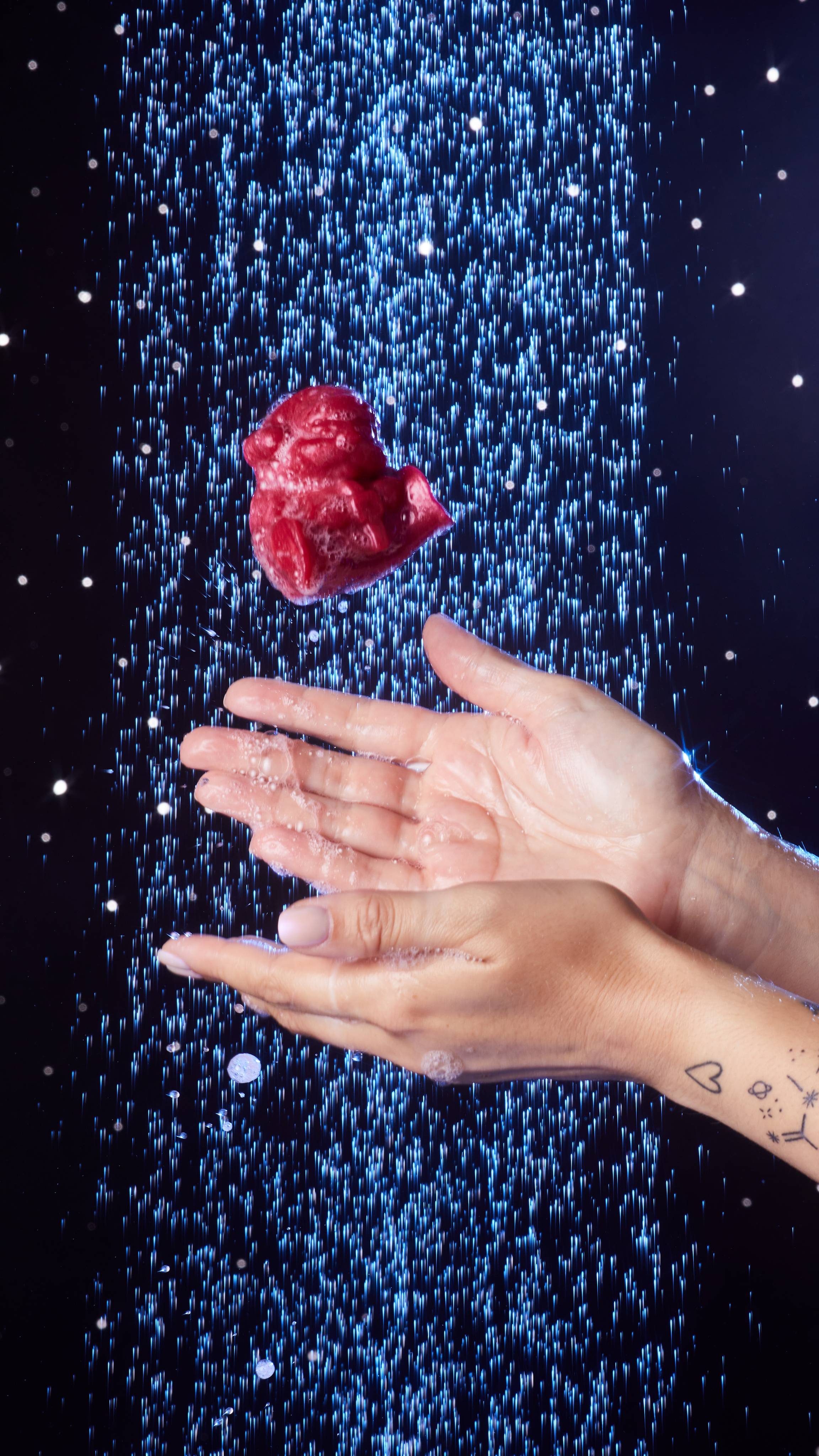 Image shows the model's hands under shower water, lathered in bubbles as they have just thrown the Bouncing Santa in the air. 