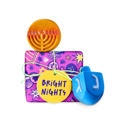 Bright Nights. A gift box wrapped in vibrant pink wrapping decorated with Hanukkah-themed illustrations of Menorahs and six-pointed Stars of David. Two themed Hanukkah products are sitting beside the box. 