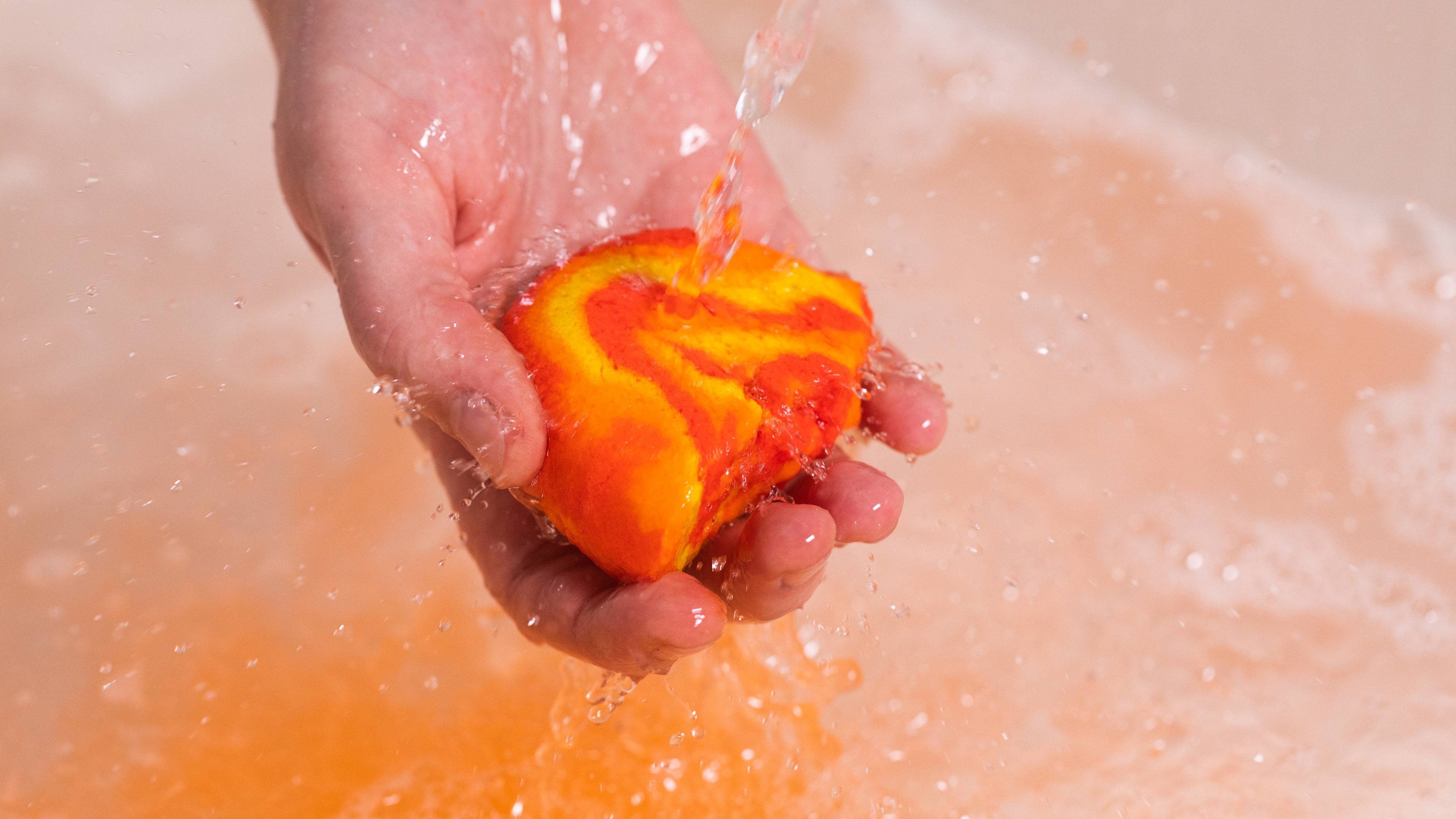 Model holds the Mini Brightside bubble bar under running water as firey-orange bubbles form below.