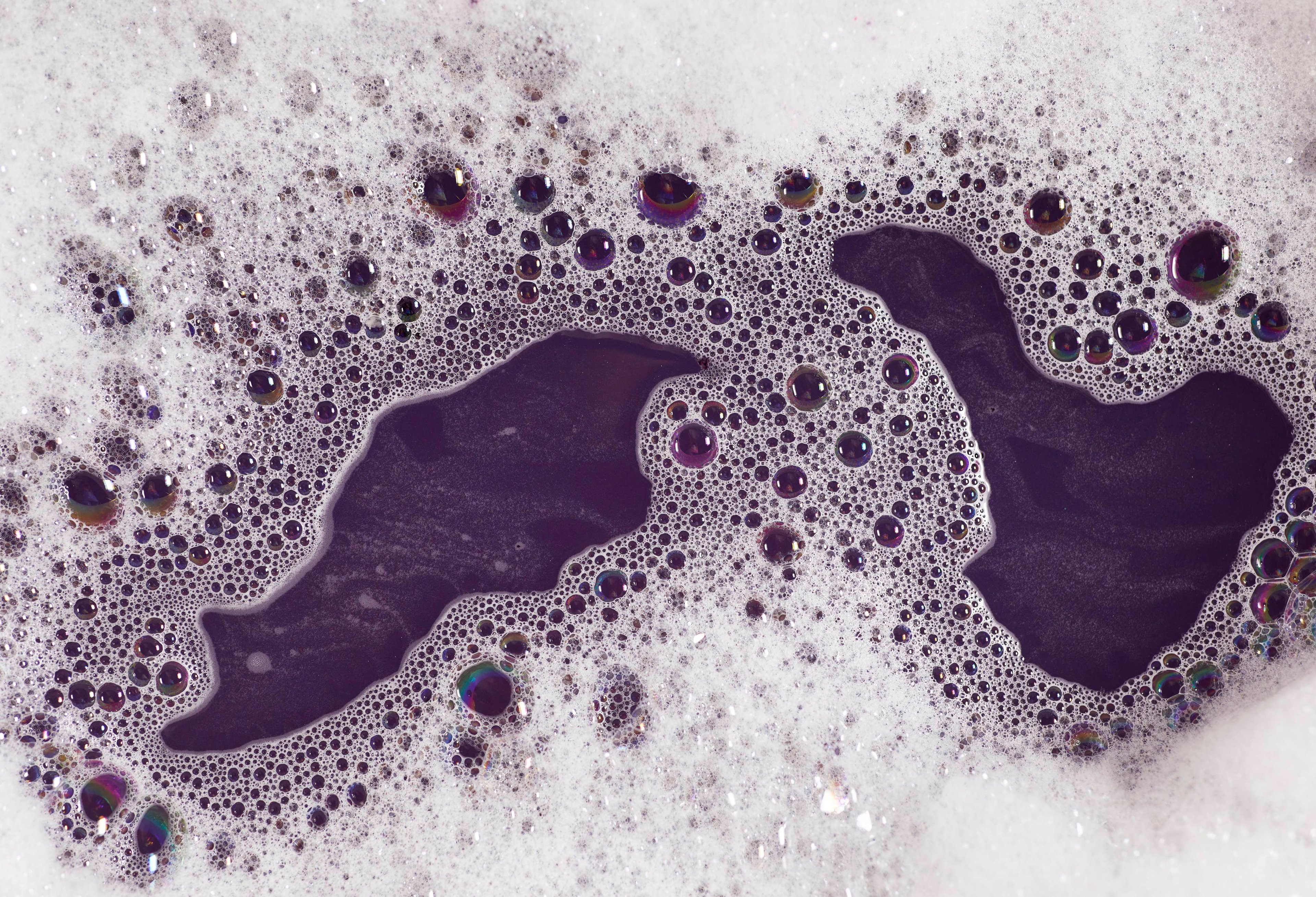 The image shows a close-up of deep, gothic, purple-coloured water surrounded by light, fluffy bubbles.