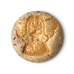 A LUSH Bûche de Noël cleanser, a solid, pale-coloured product with red specks, is shown against a light gray background. An angel is embossed on the top, covered in shimmering gold glitter.