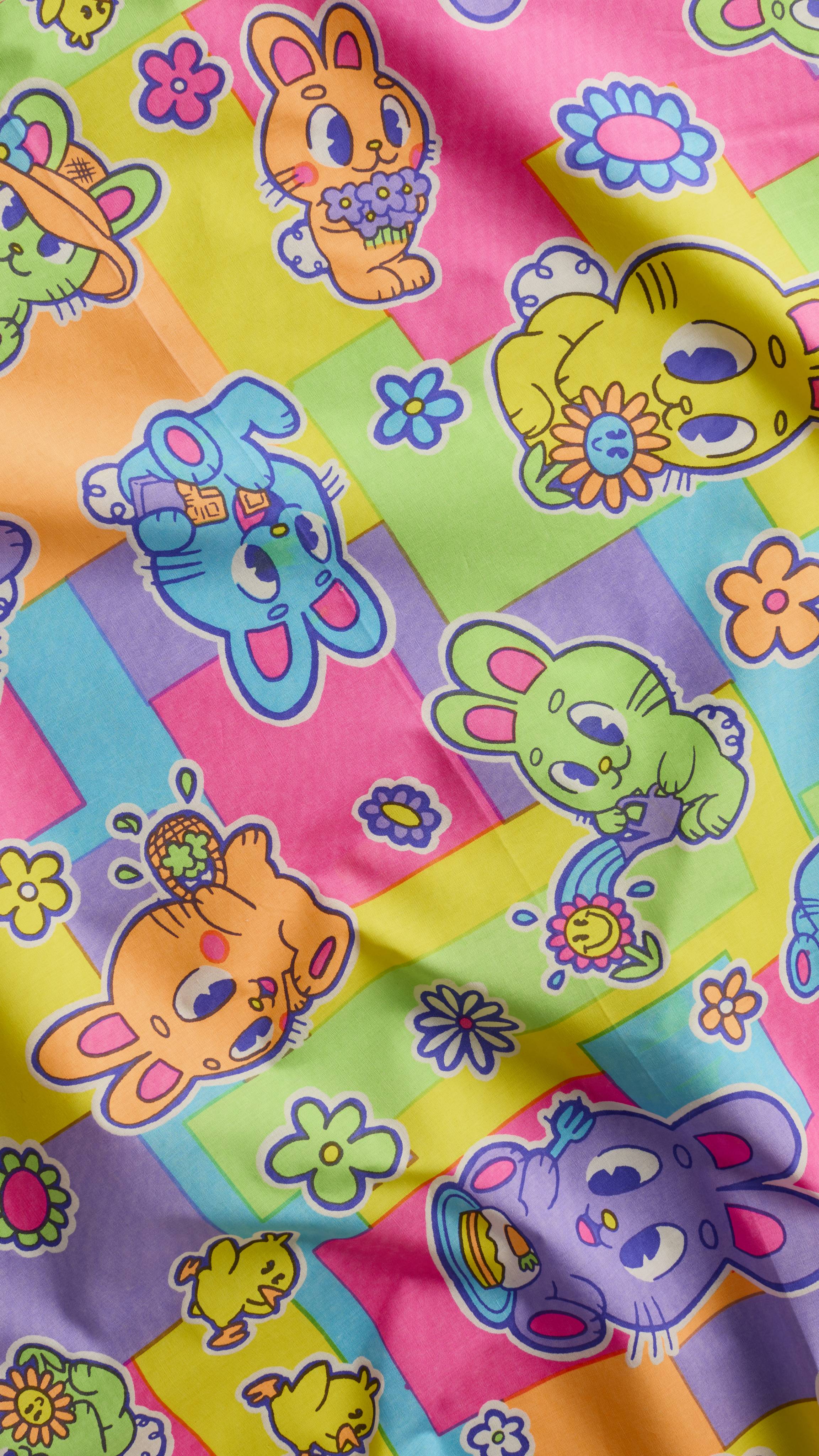 A super close-up of the vibrant "Bunnies Picnic" knot wrap featuring a repeat pattern of colourful, cartoon-style bunnies and chicks amidst flowers. The design uses a bright palette of pink, yellow, blue, and green.