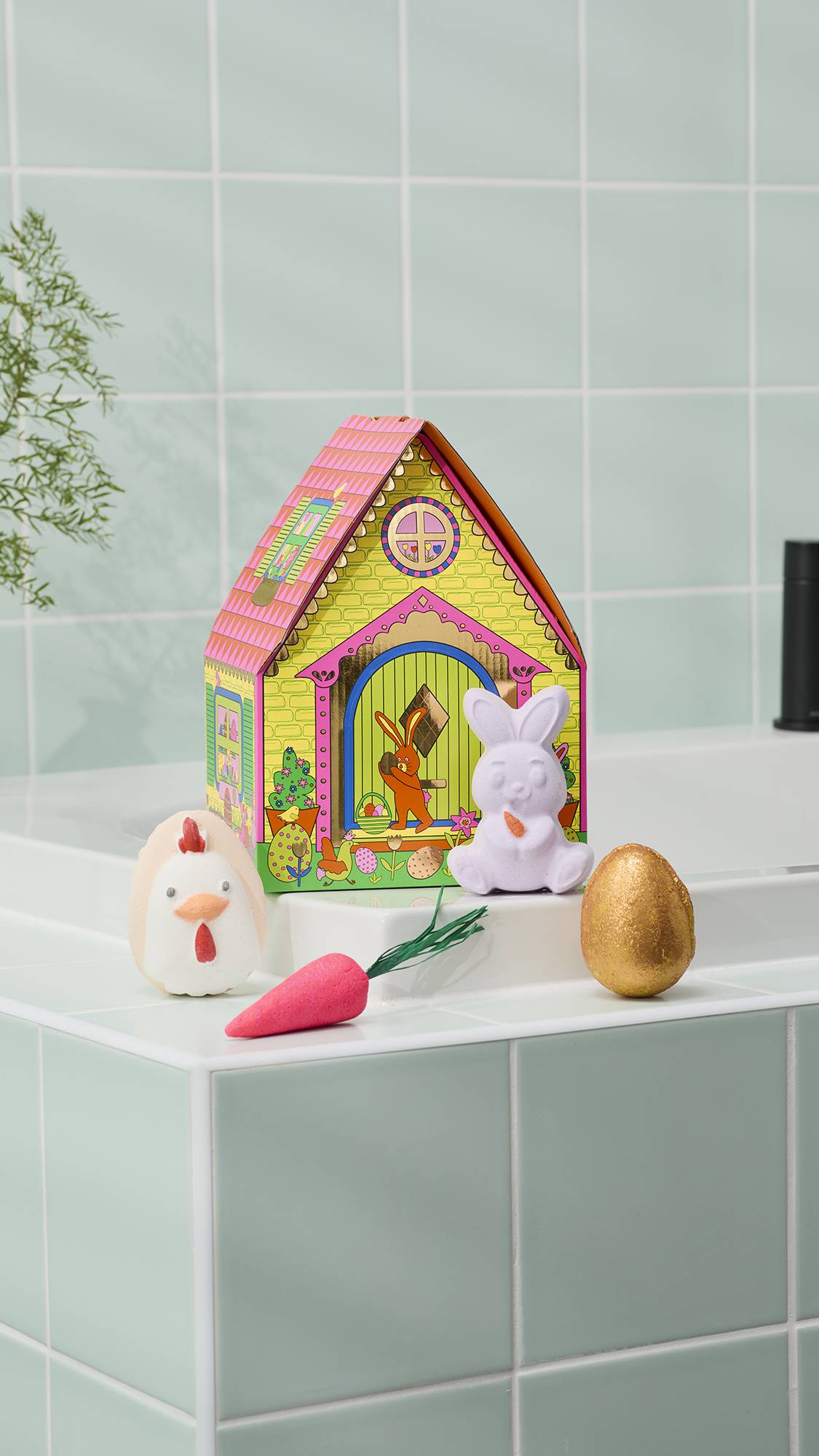 A "Bunny Cottage" Easter gift set is displayed on the edge of a white bathtub. It features a house-shaped gift box with bunny illustrations. In front of the box sit the four included Easter-themed bathing products, against green tiles.