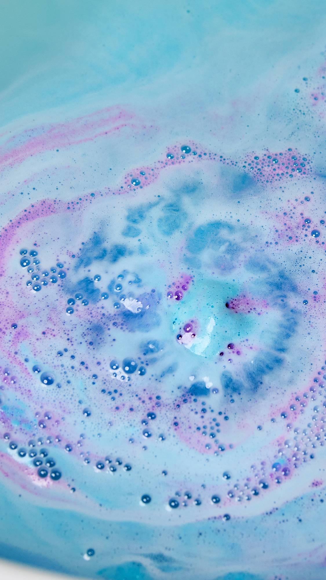 The Bunny Moon bath bomb has nearly fully dissolved erupting in a bright blue foam with flashes of pink and purple.